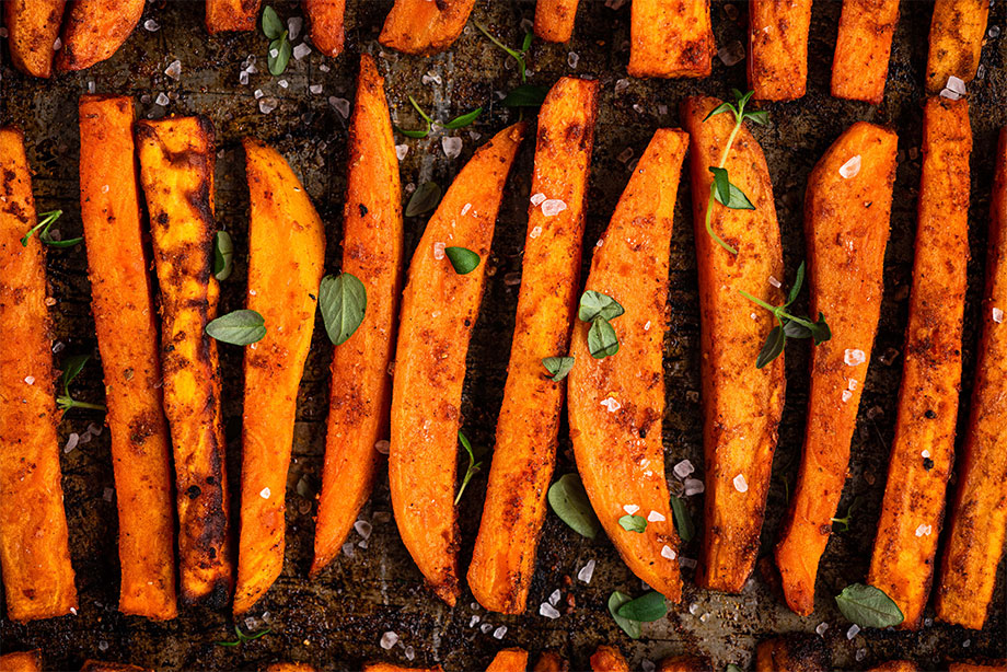 Grilled sweet potato wedges arranged in rows with herbs and sea salt on dark surface.