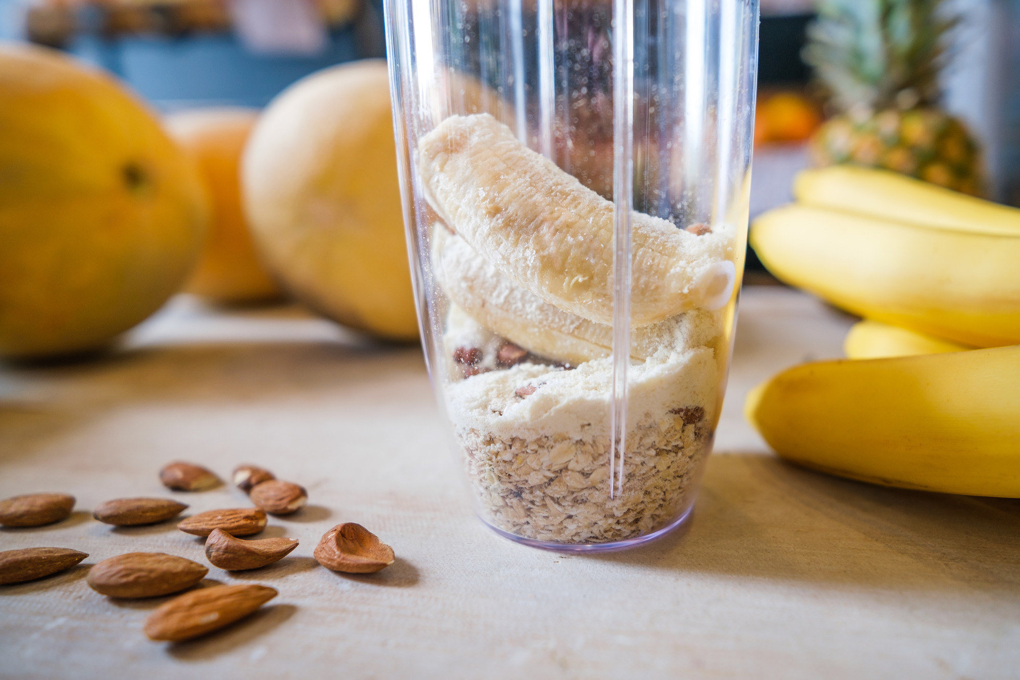 Blender with almond butter being made, almonds and fruits on kitchen counter
