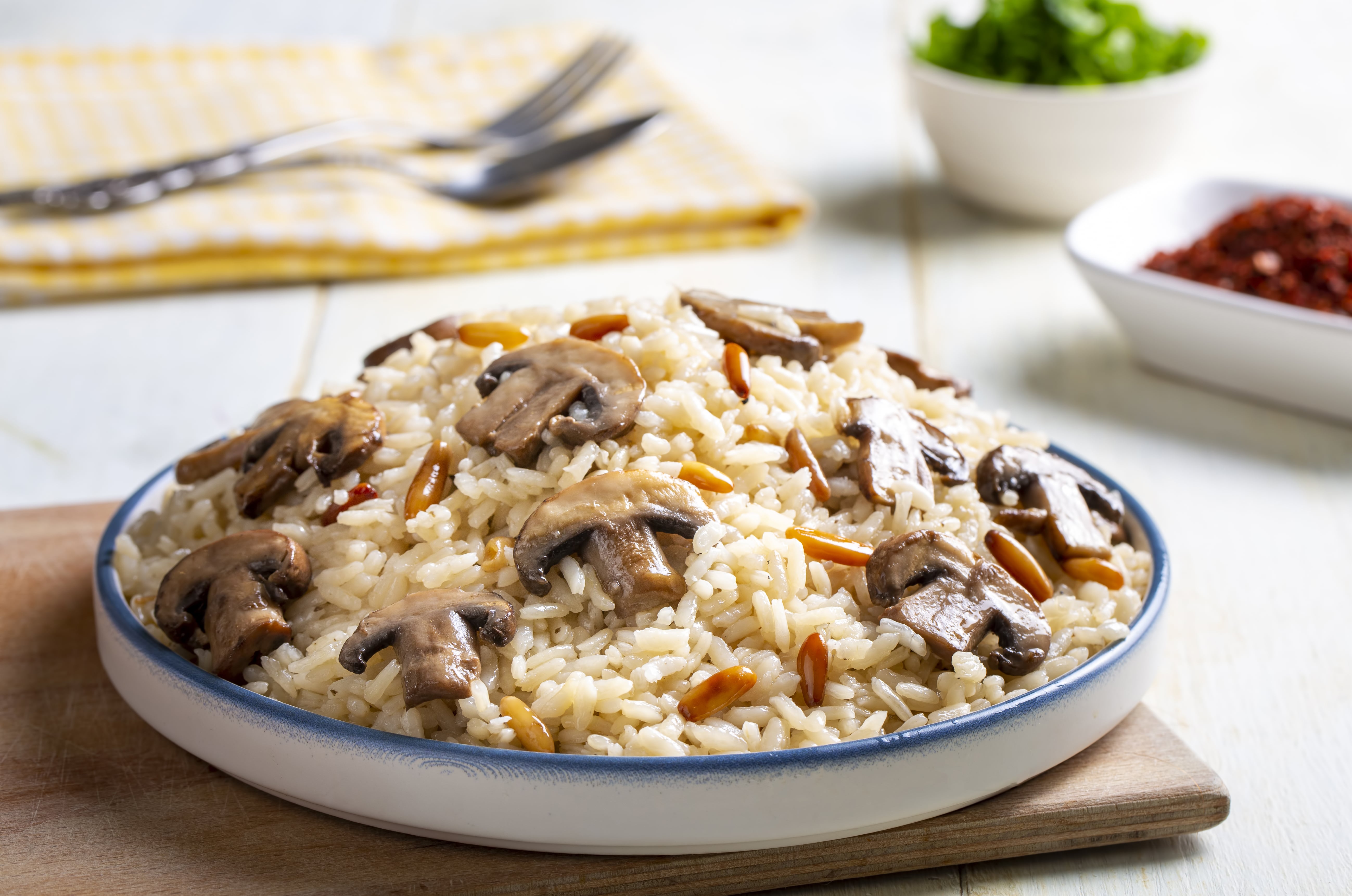 Bowl of rice with sliced mushrooms and vegetables on wooden board with utensils
