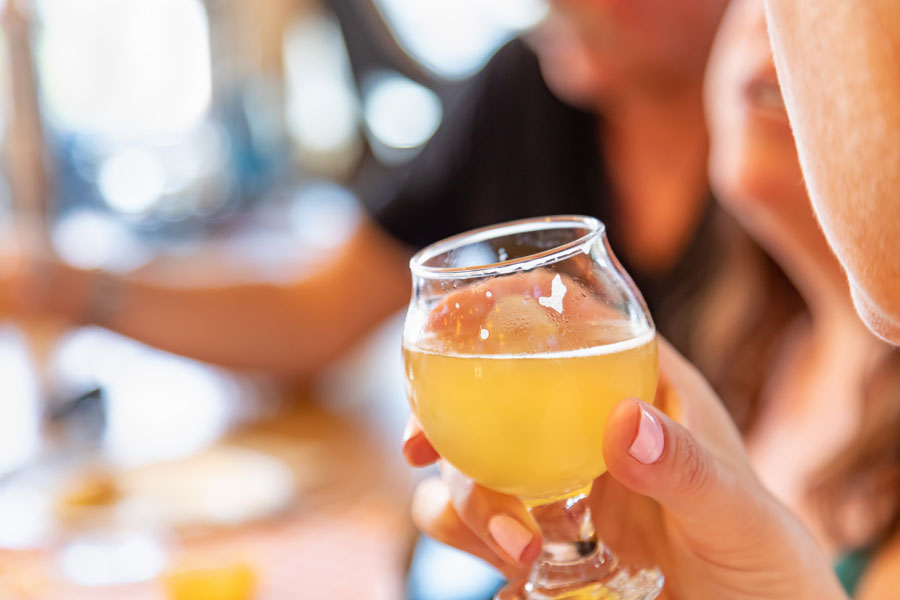 Person holding glass of golden beer outdoors in bright sunlight