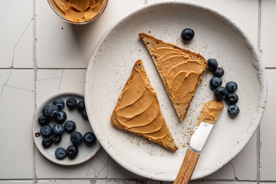 Peanut butter spread on toast slices with blueberries on white speckled plates
