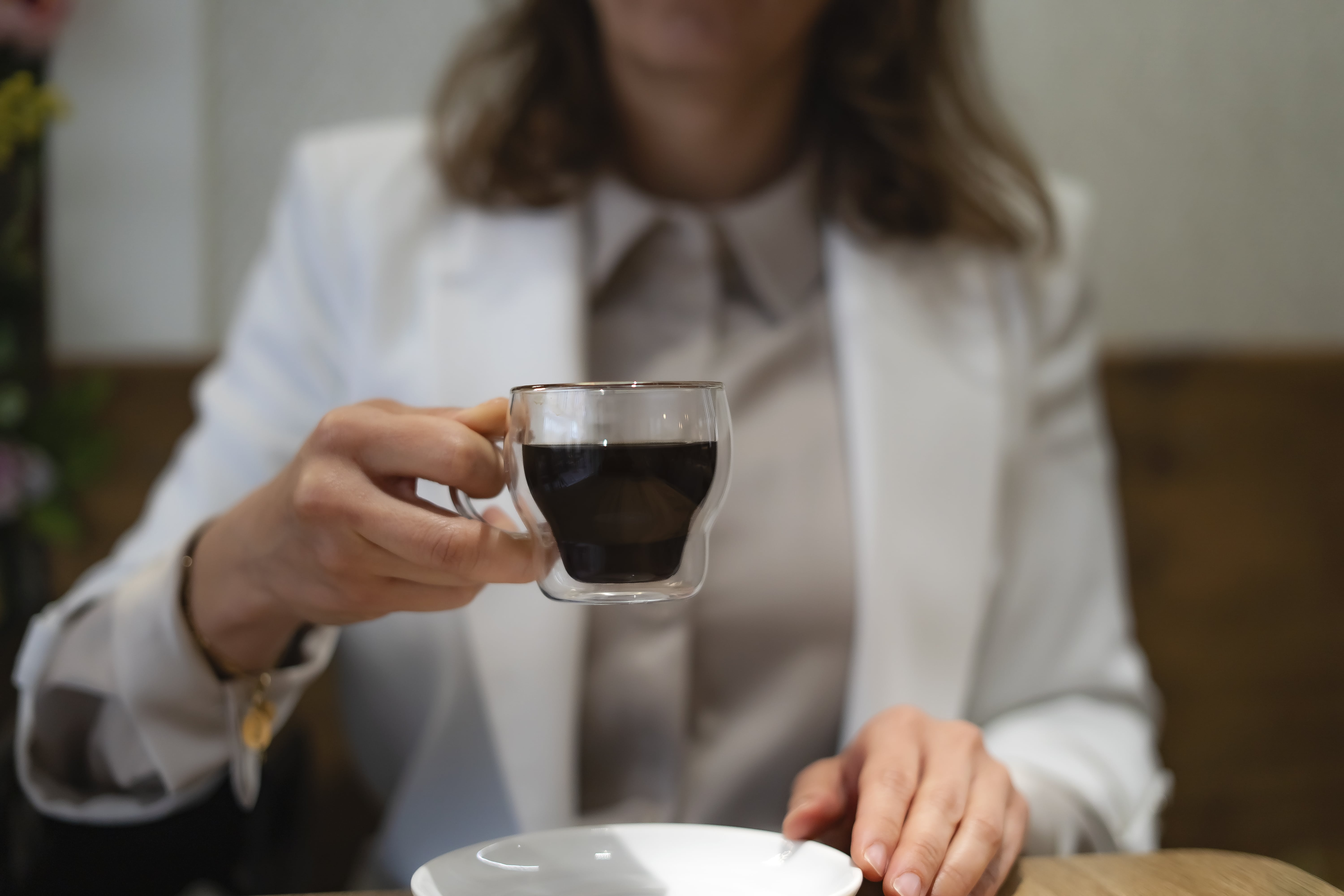 Woman in white shirt holding glass of black coffee at table