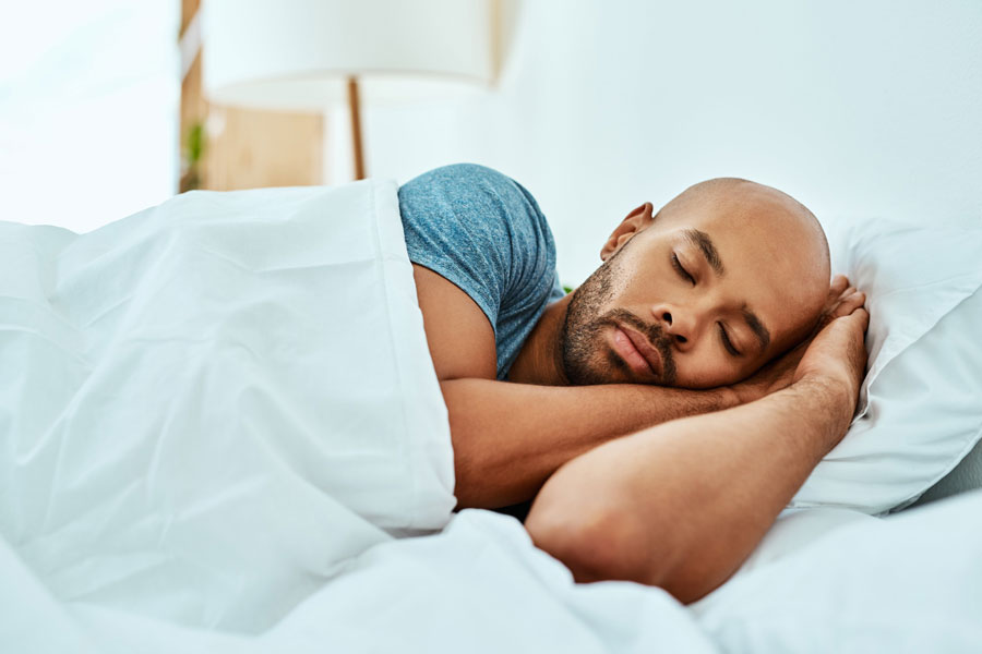 Man sleeping peacefully in bed with white bedding and blue shirt