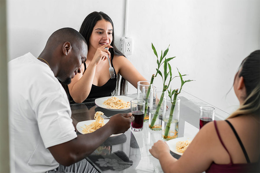Three people sharing a meal together at a table with drinks and potted plant