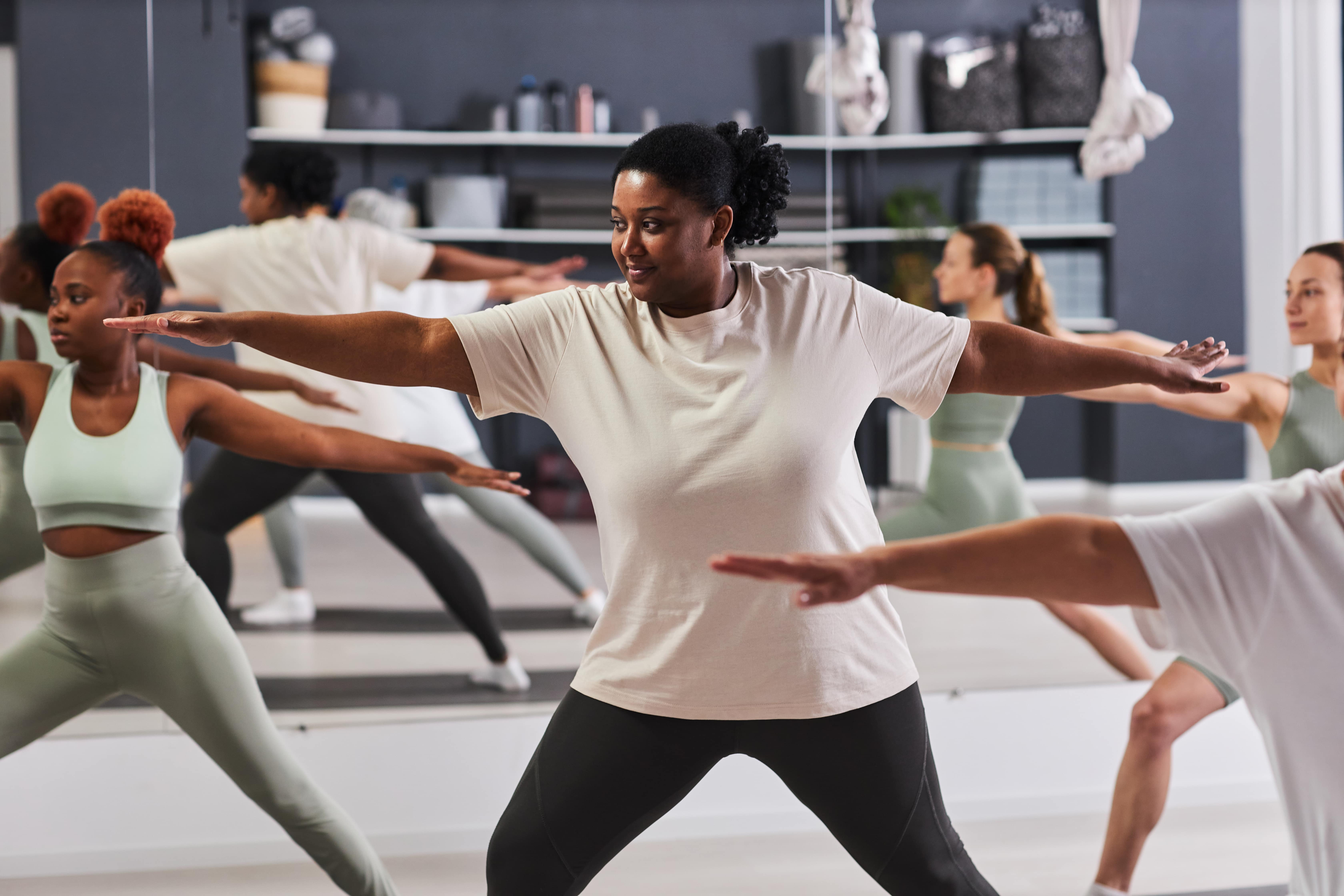 Group fitness class instructor leading diverse participants in a workout with arms extended in motion