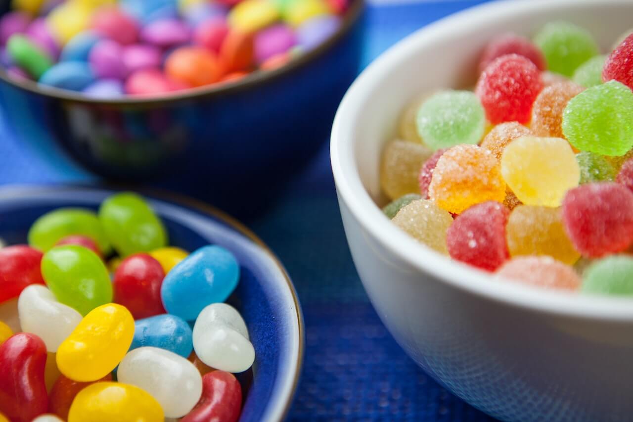 Colorful candies and gummy sweets in blue and white bowls on blue surface