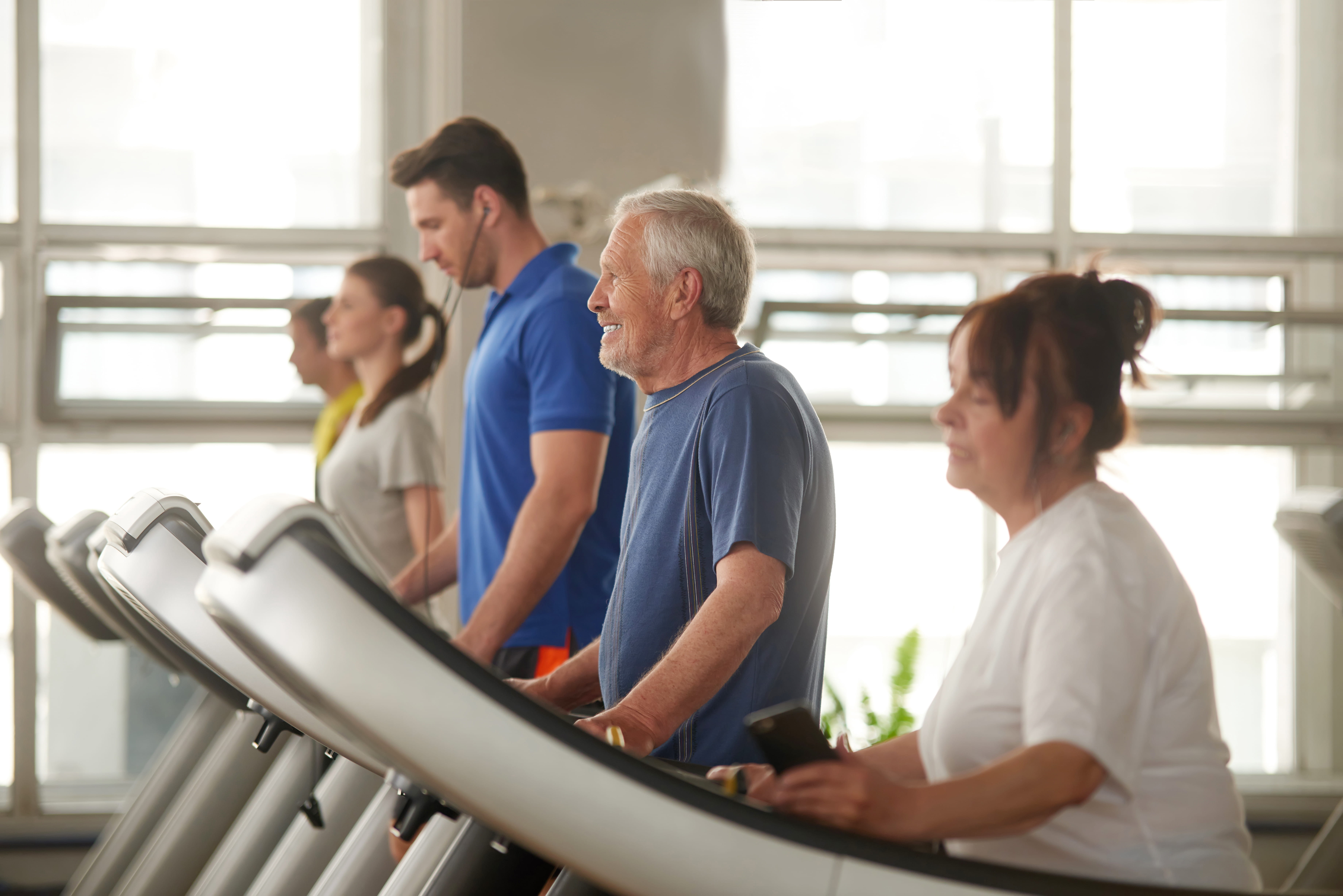 Group of people exercising on treadmills in a bright gym with large windows