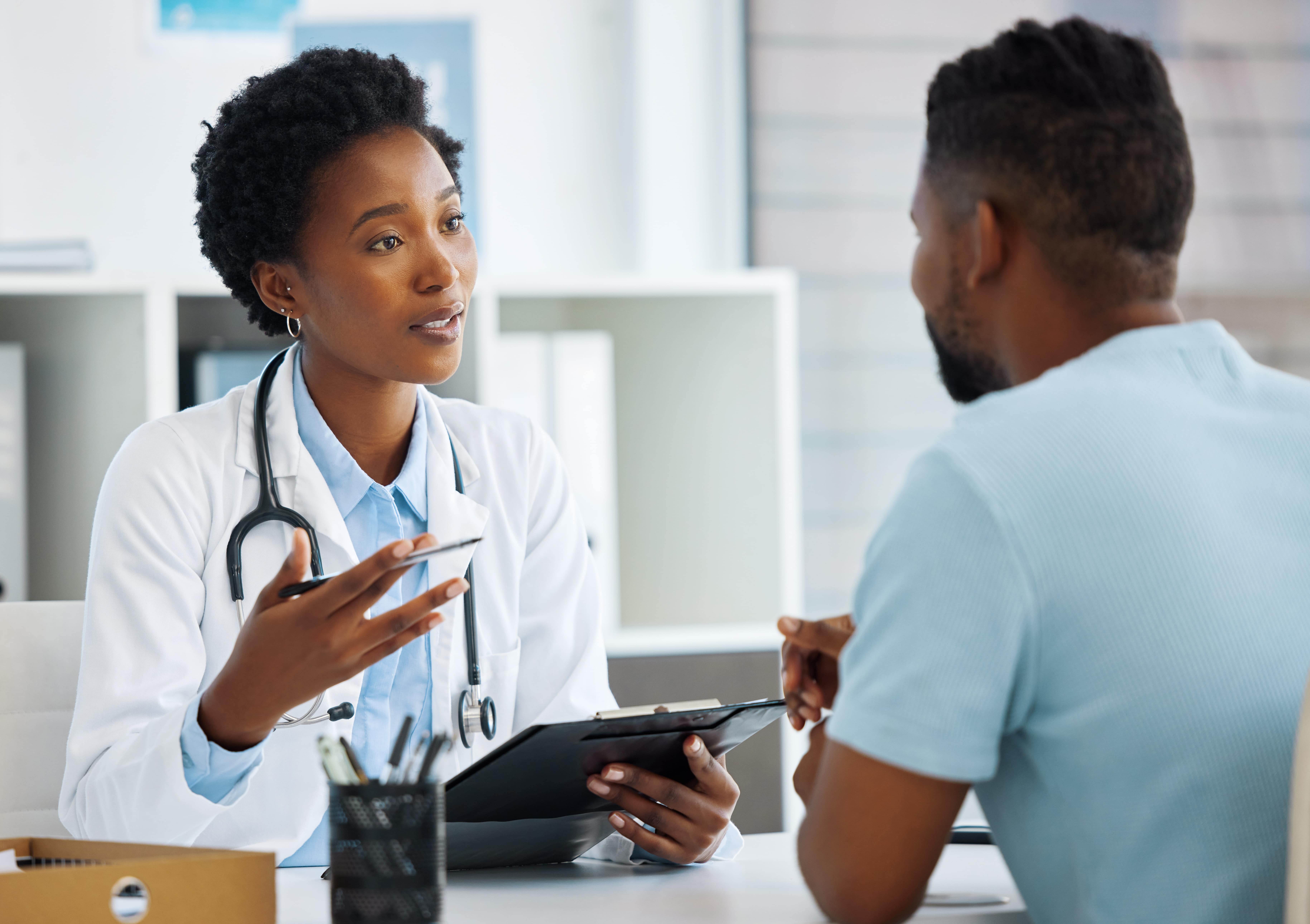 Female doctor with stethoscope discussing test results with male patient in clinic office.