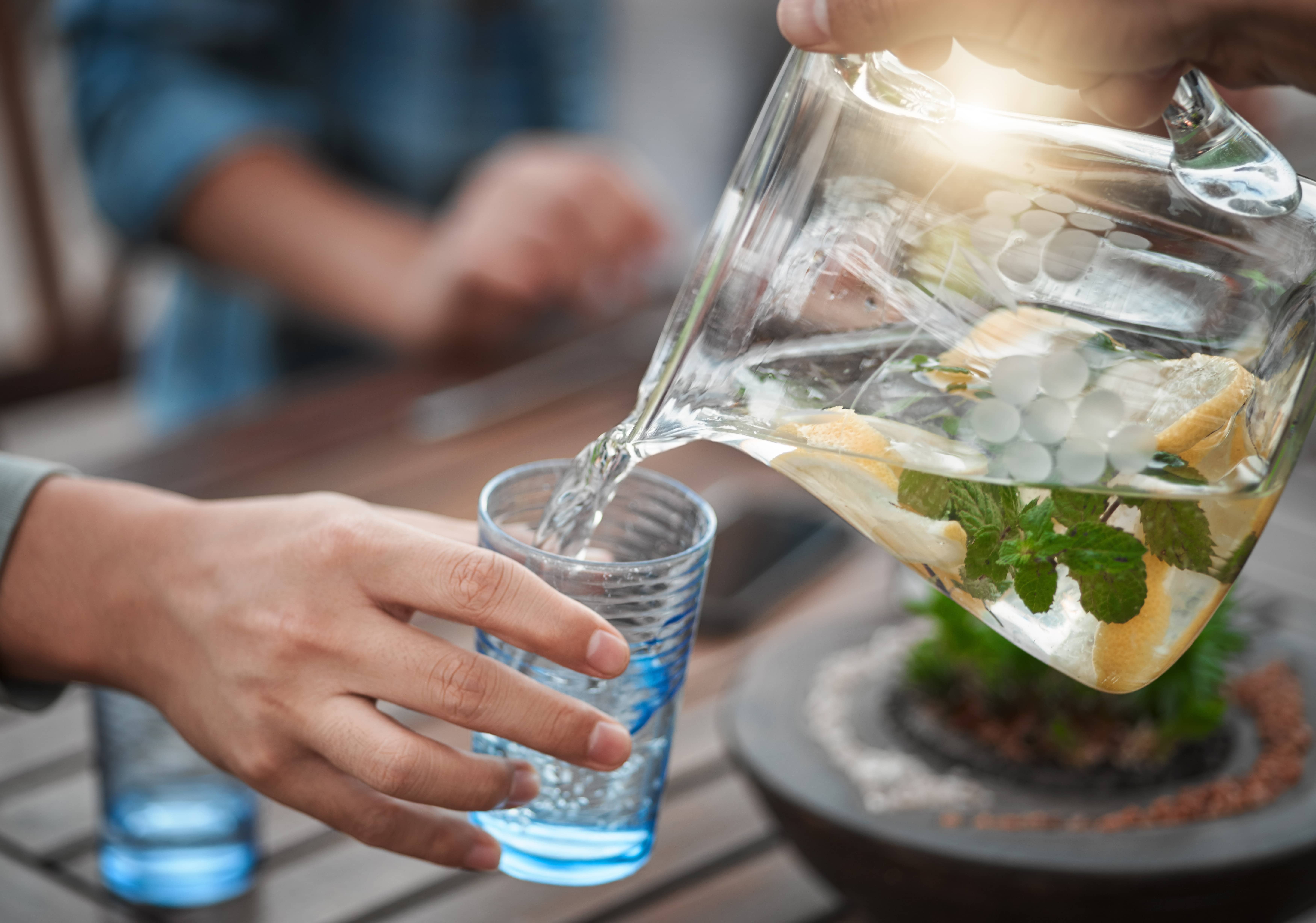 Person pouring infused water with lemon and mint into a glass