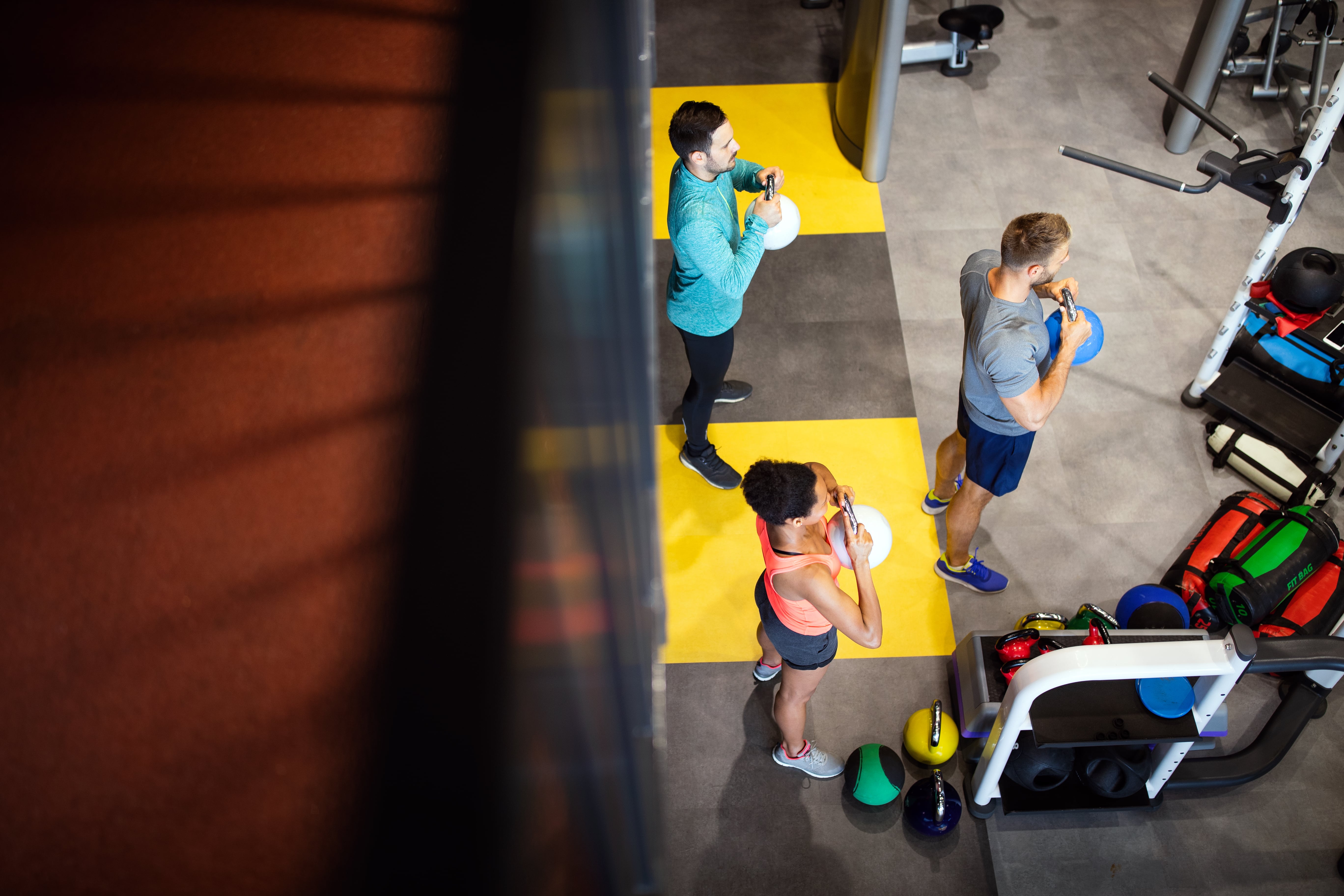 Three people exercising in a gym with kettlebells on yellow and black mats.