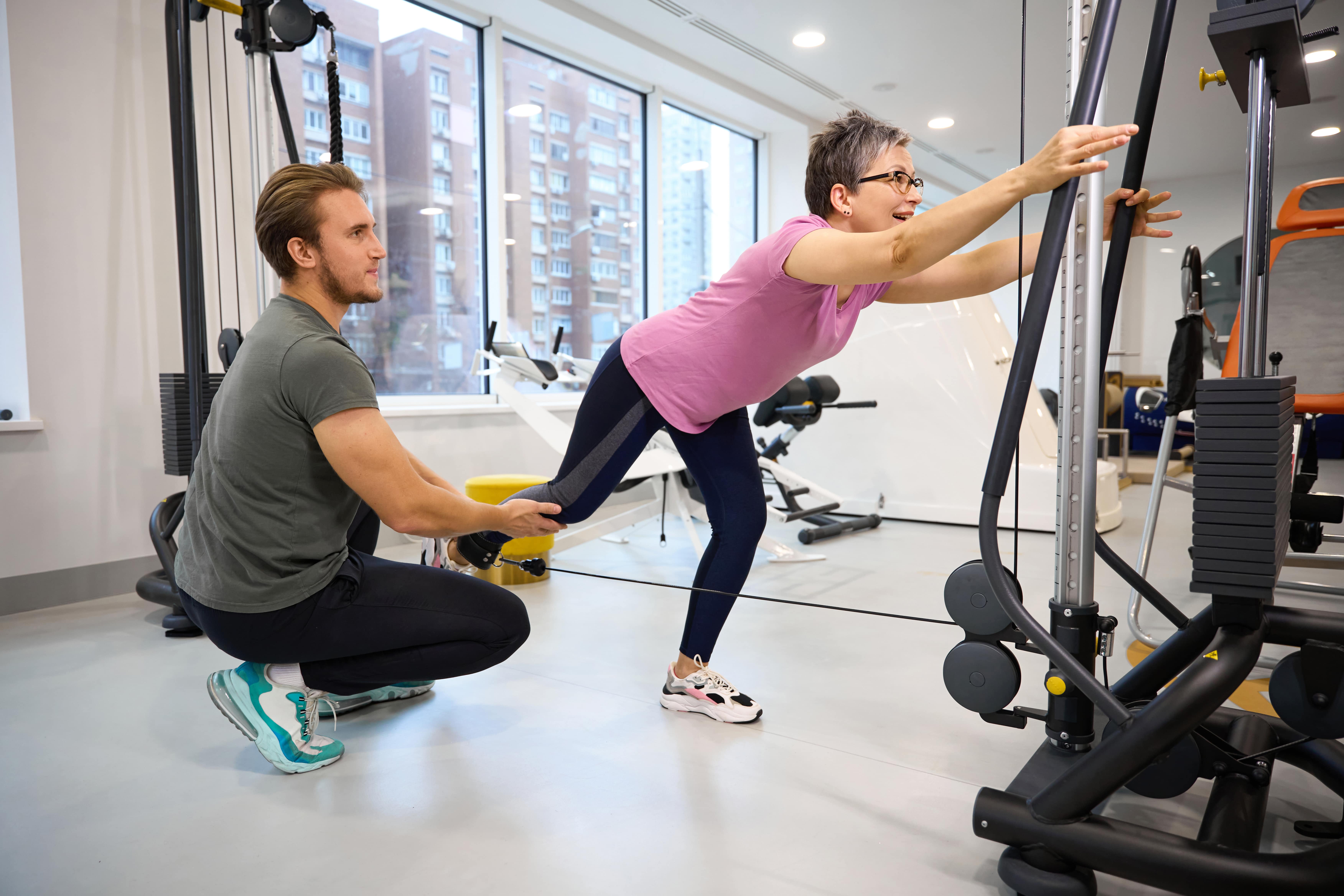 Personal trainer assists woman doing resistance band exercise in modern gym