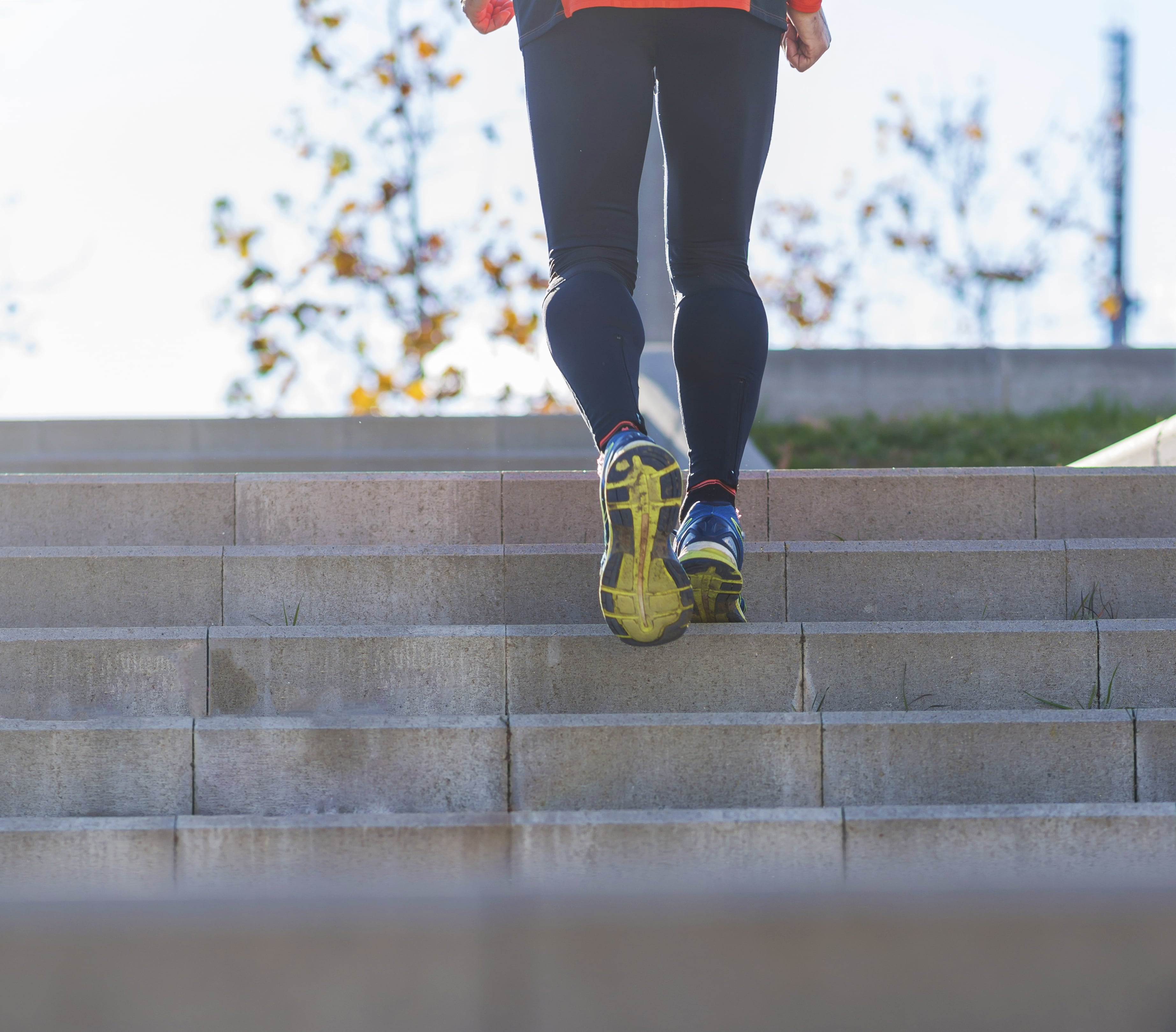 Runner in black leggings ascending concrete stairs outdoors during fall season