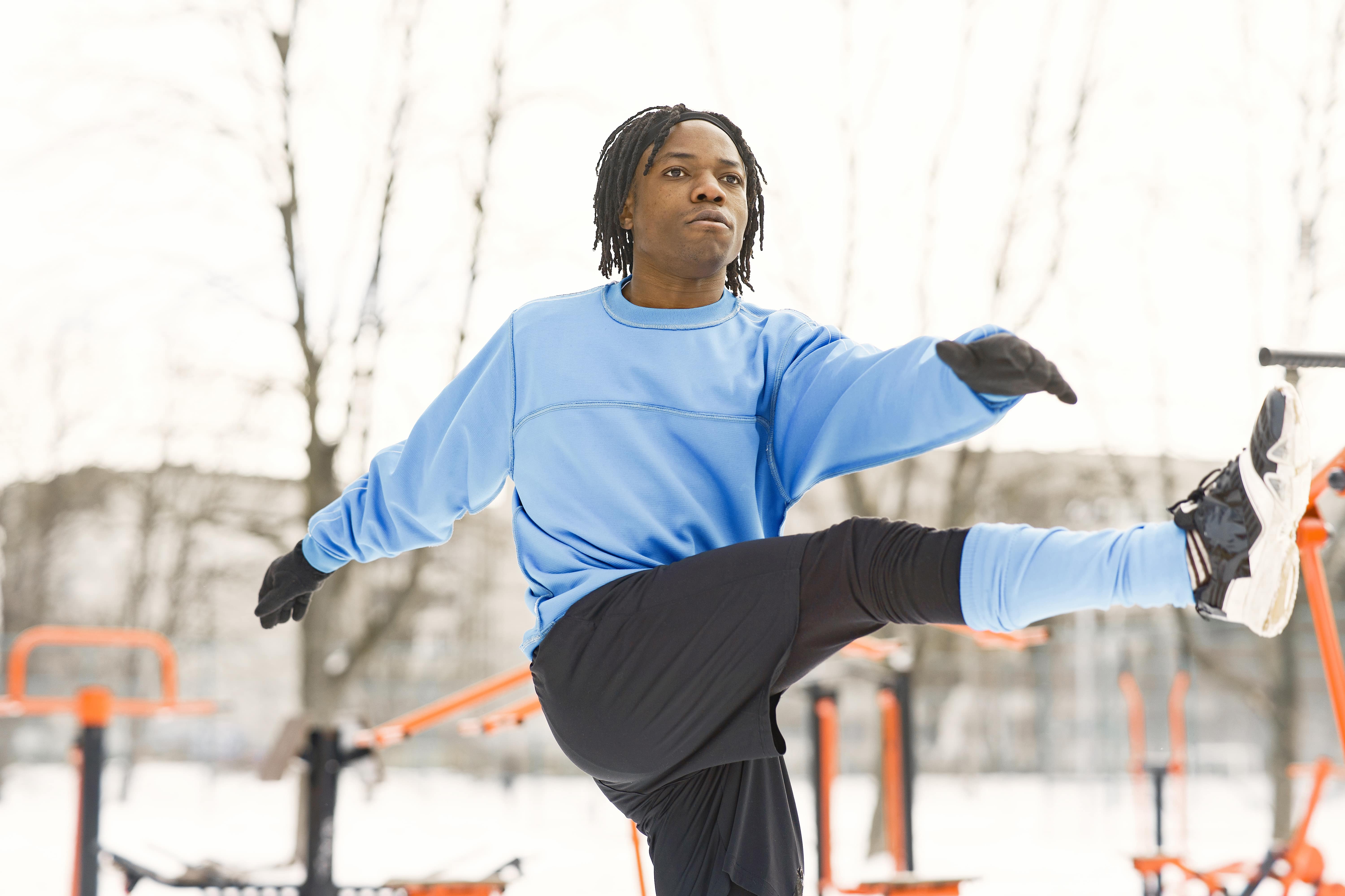 Man in blue sweatshirt stretching with raised leg at outdoor fitness park