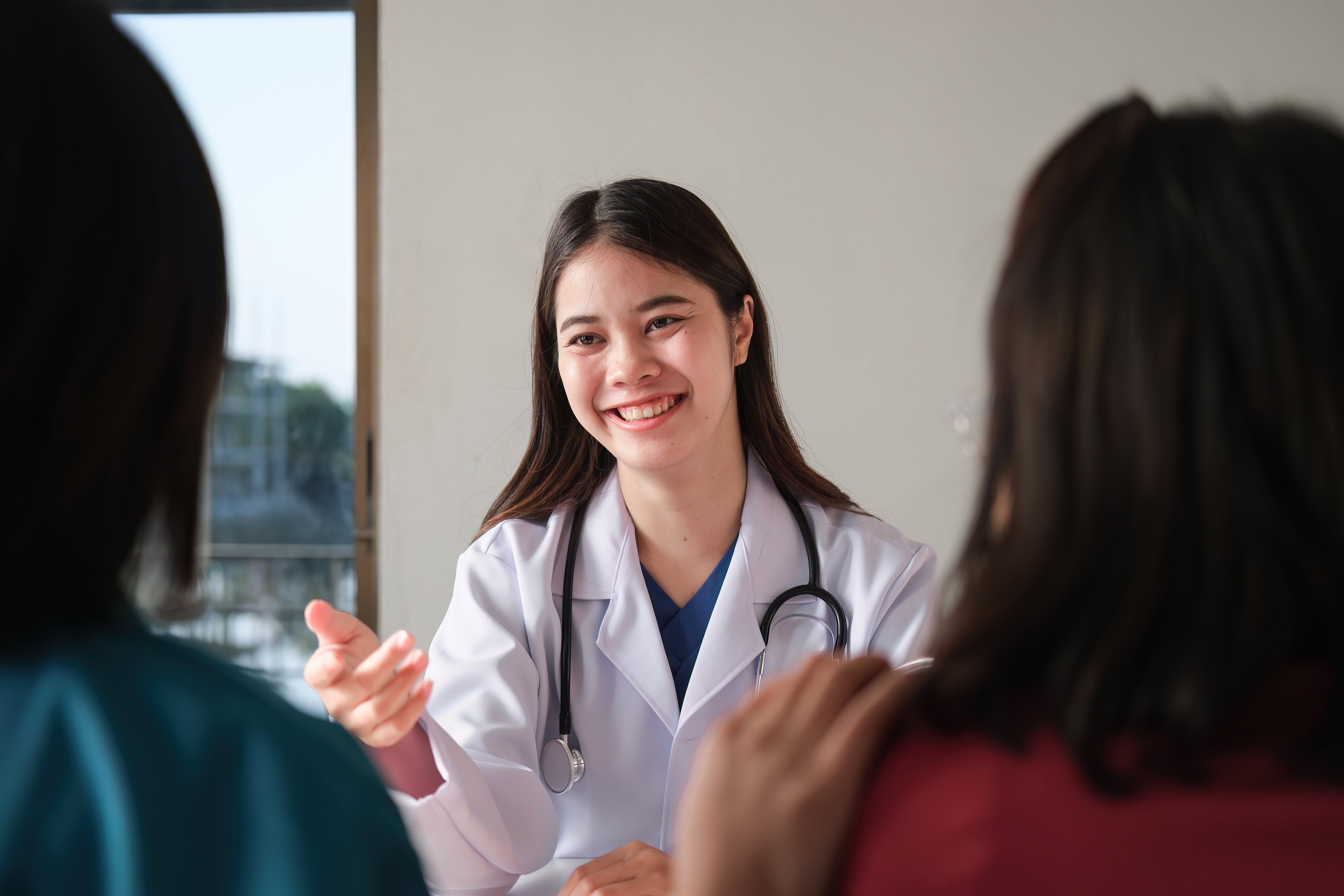 Female doctor in white coat smiling, speaking with patients in medical office