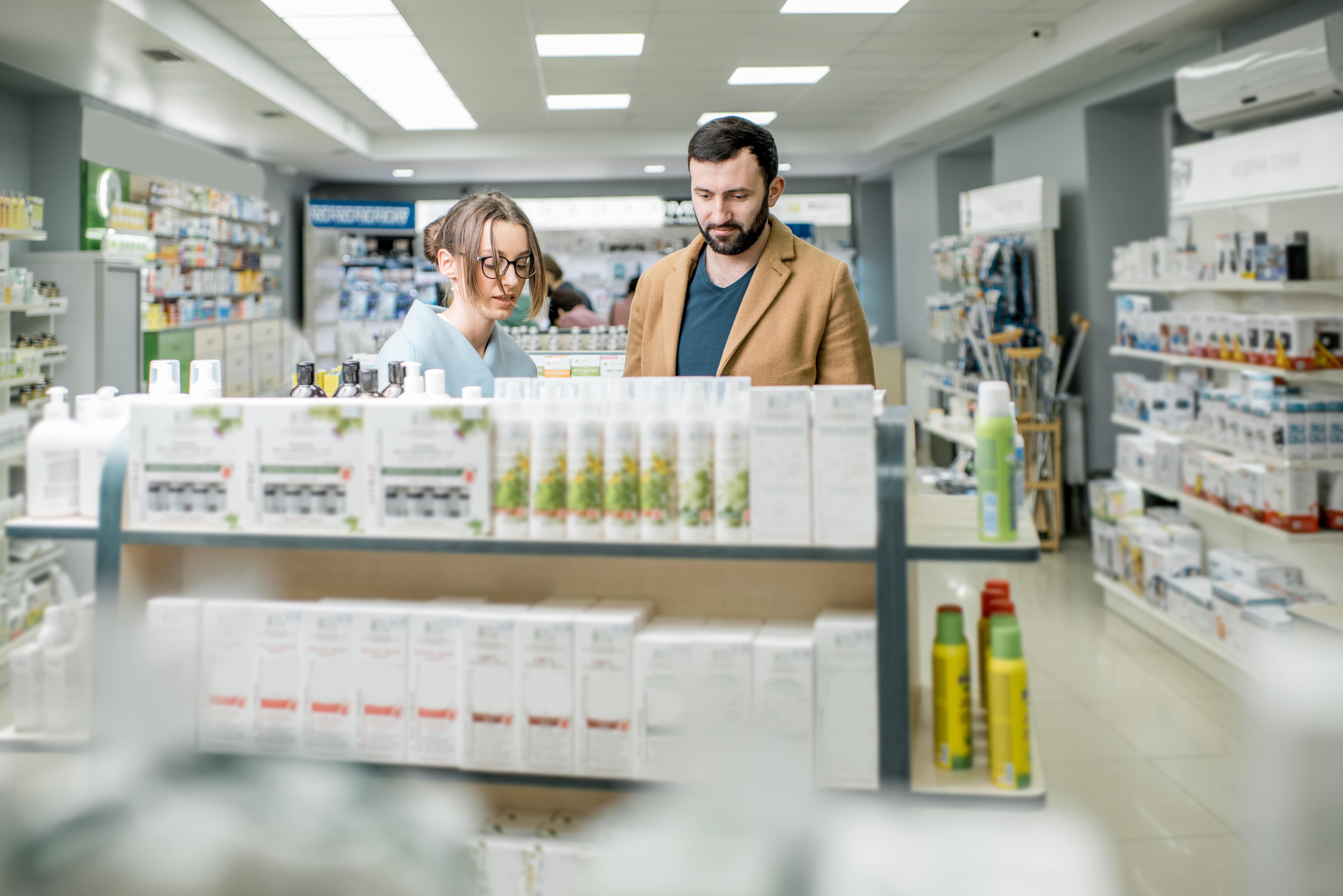 Female pharmacist and male customer browsing products at pharmacy counter display
