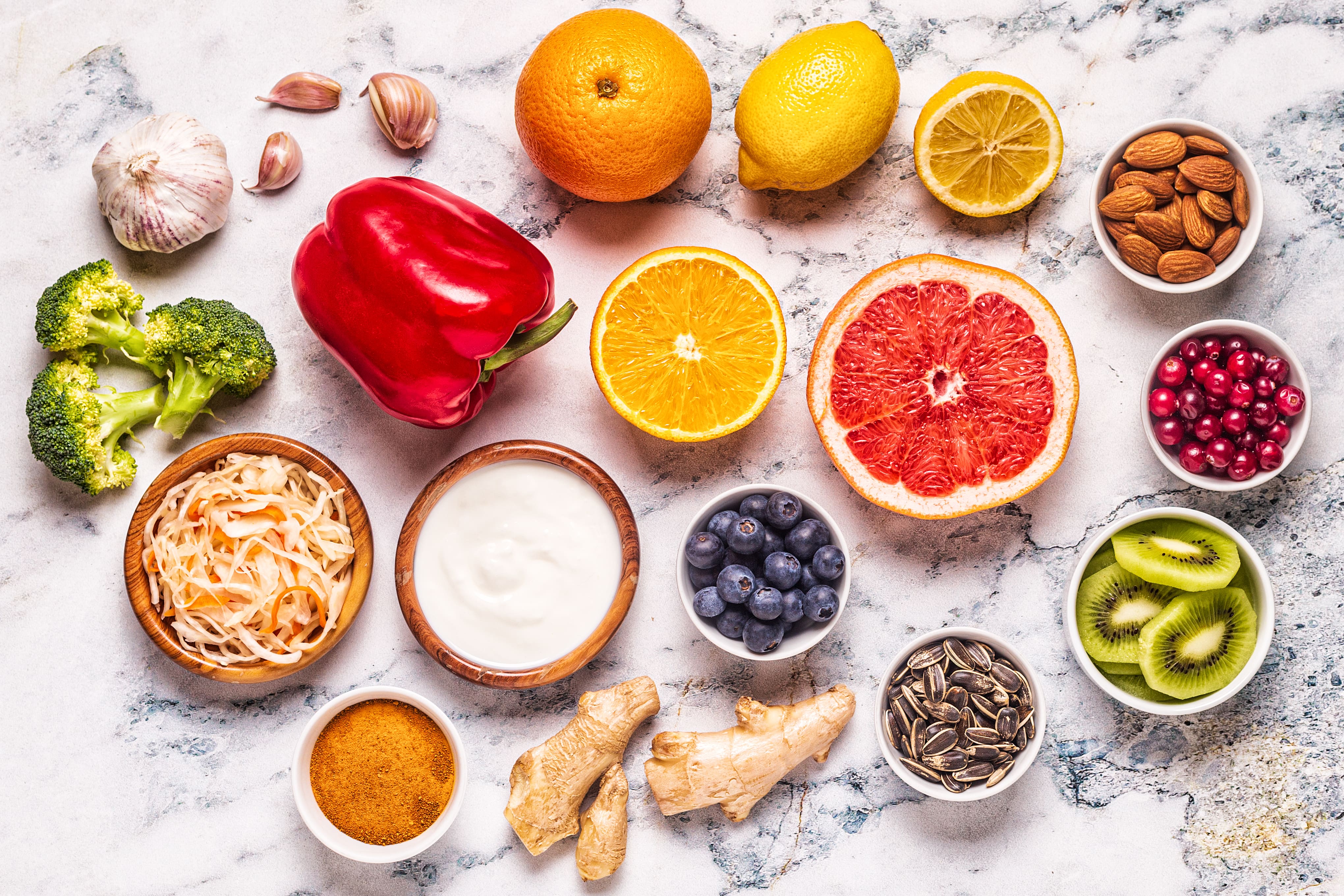 Colorful healthy foods arranged on marble: citrus fruits, vegetables, nuts, berries, and yogurt overhead view.