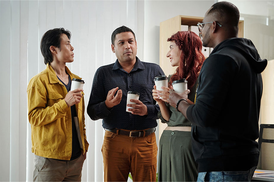 Four diverse professionals having a casual coffee break and conversation in an office.