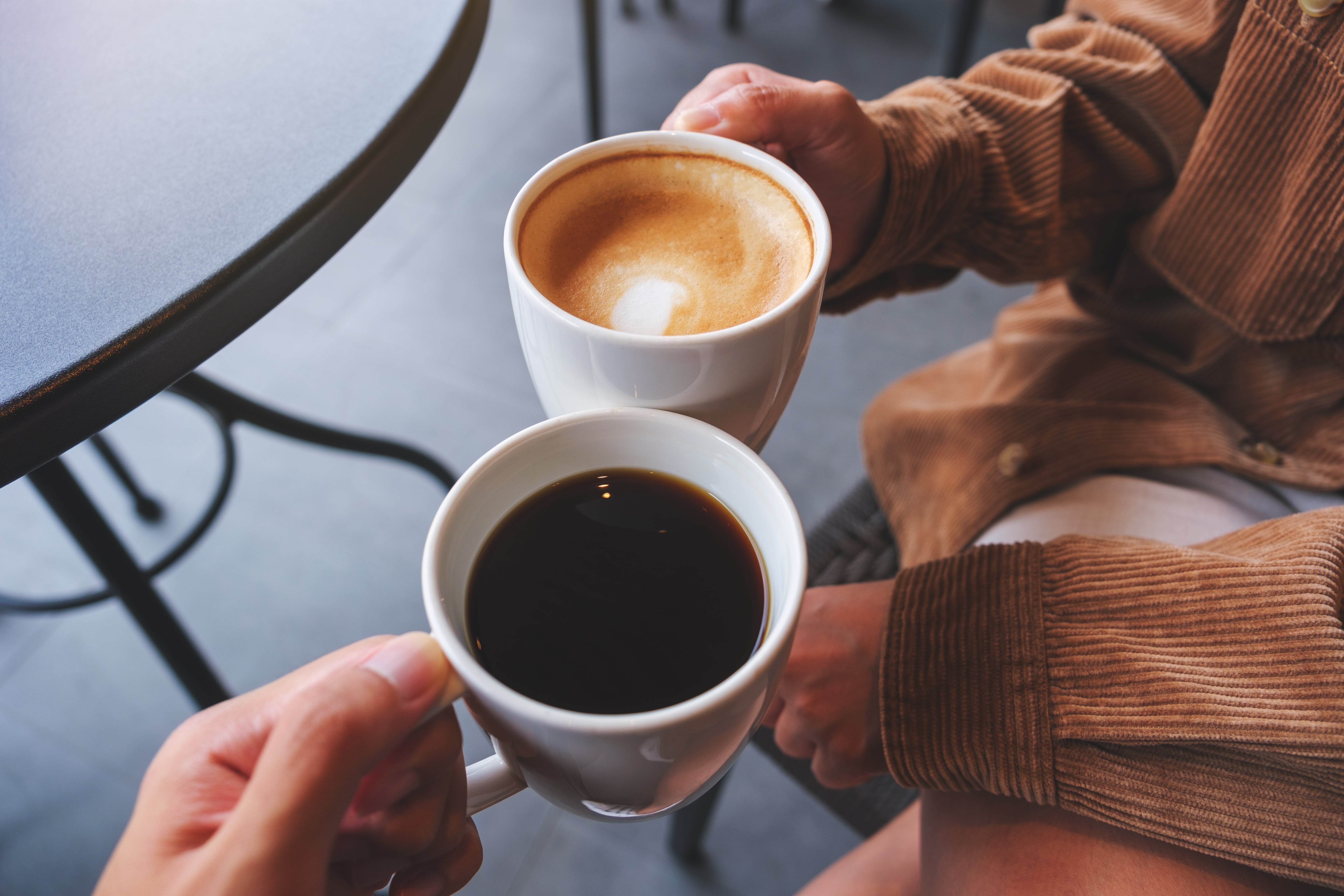 Two people holding cups of coffee and latte with latte art outdoors
