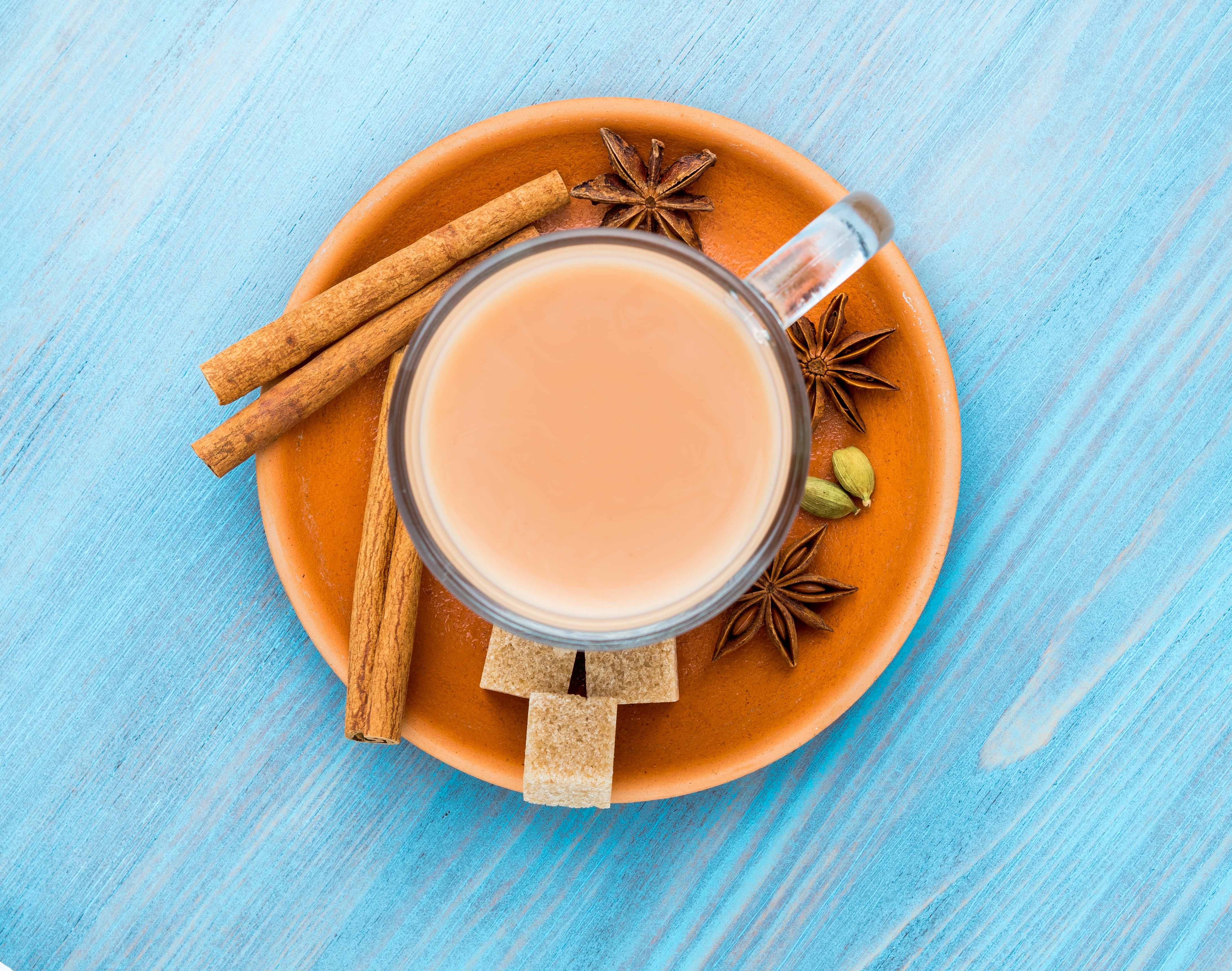 Chai tea in glass mug surrounded by cinnamon sticks, star anise, and cardamom pods
