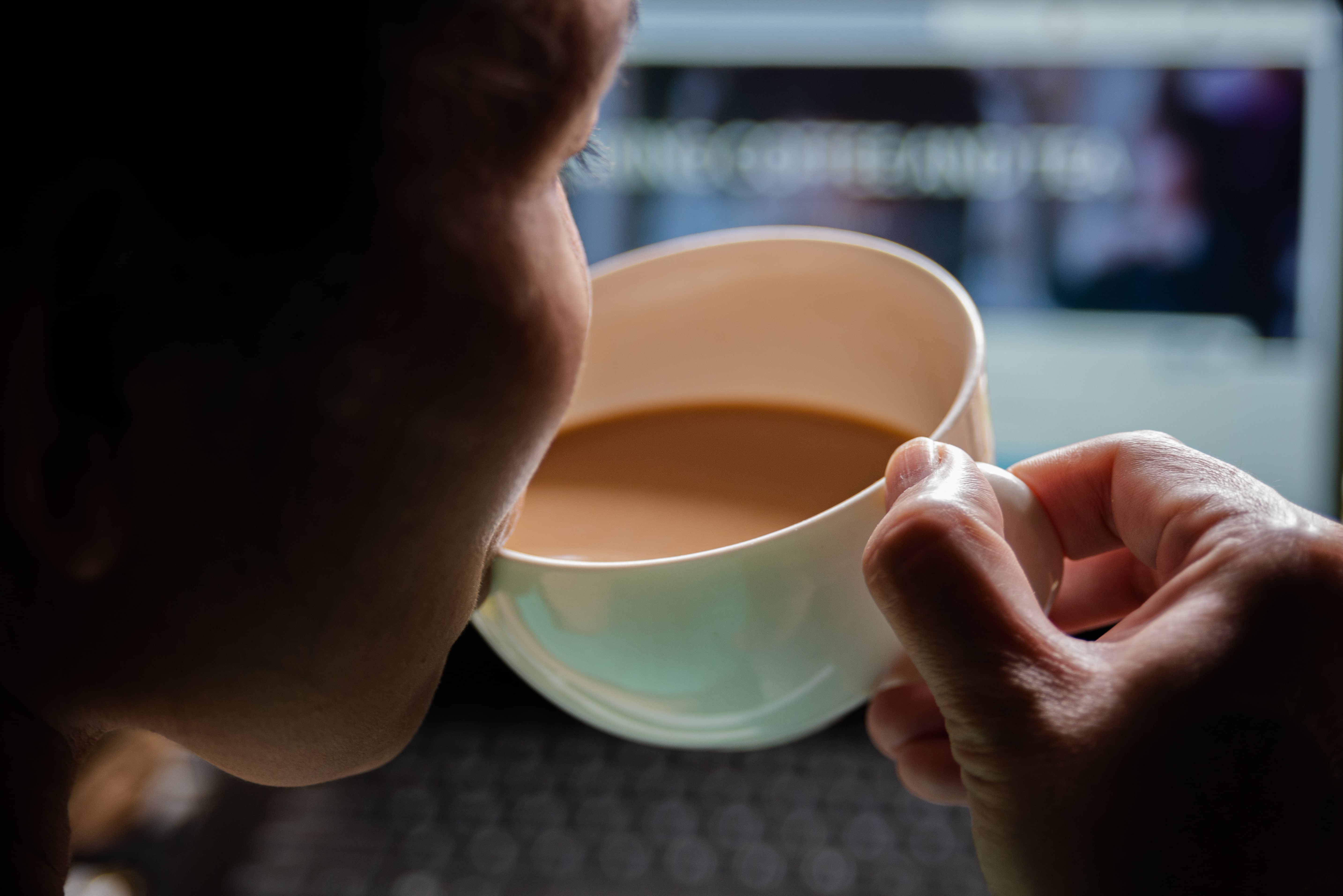 Person holding white cup of coffee with blurred office background
