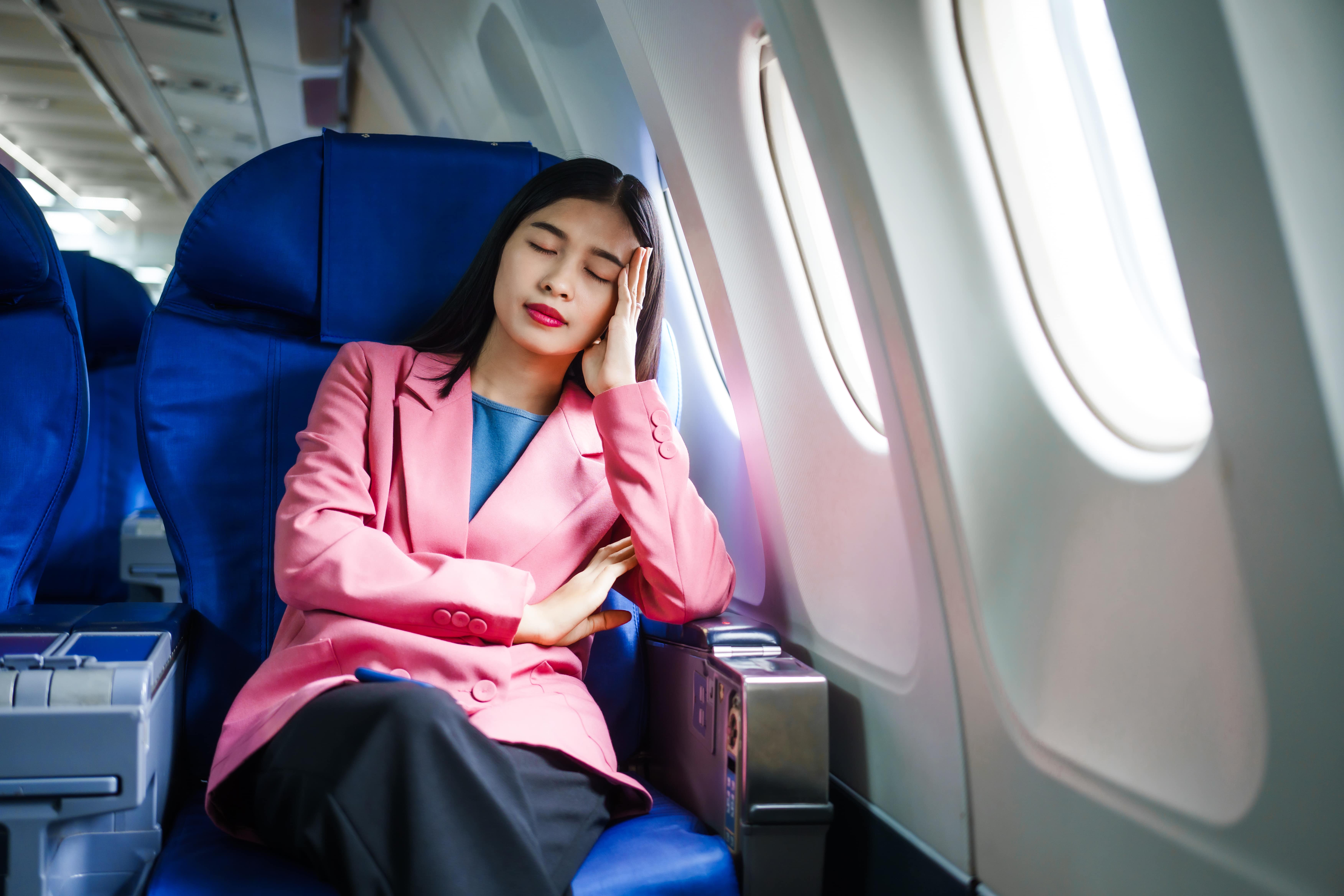 Woman in pink blazer resting on airplane seat near window