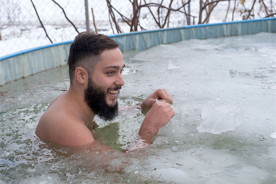 Man smiling while bathing in icy frozen pool water during winter