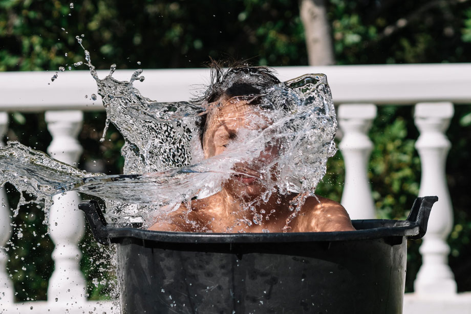 Man splashing water in black bathtub outdoors with white railing background