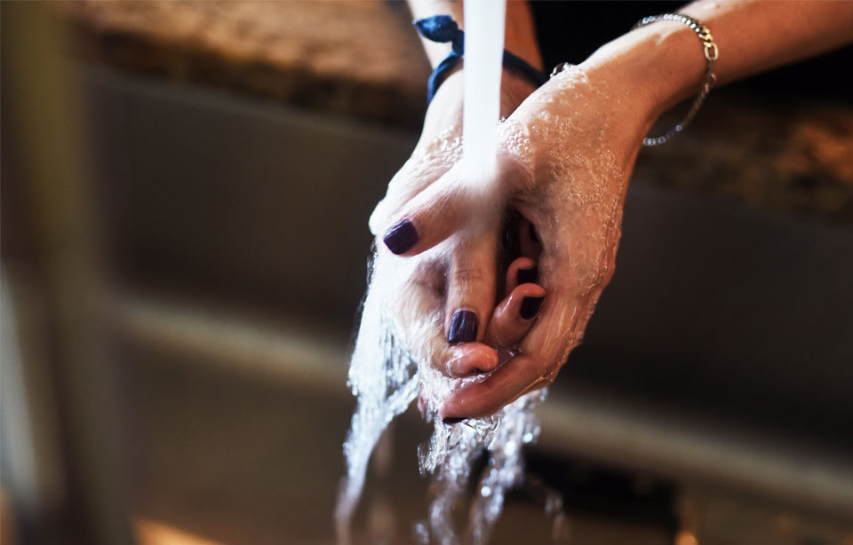 Two hands rinsing under flowing water, wearing nail polish and bracelets.
