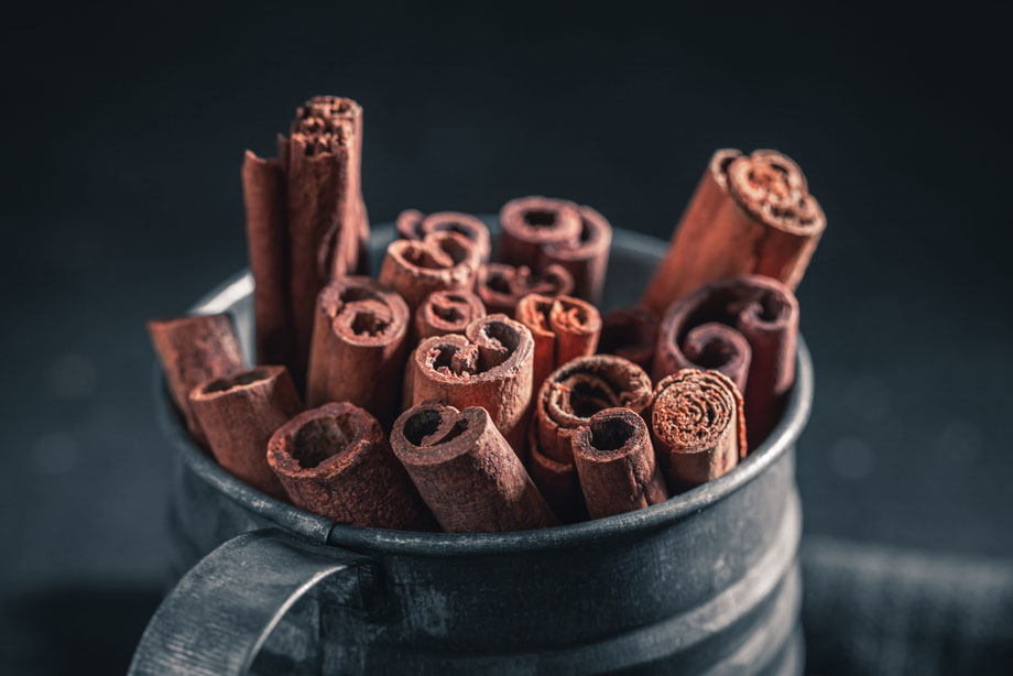 Bundle of cinnamon sticks arranged in a dark ceramic bowl on blue background