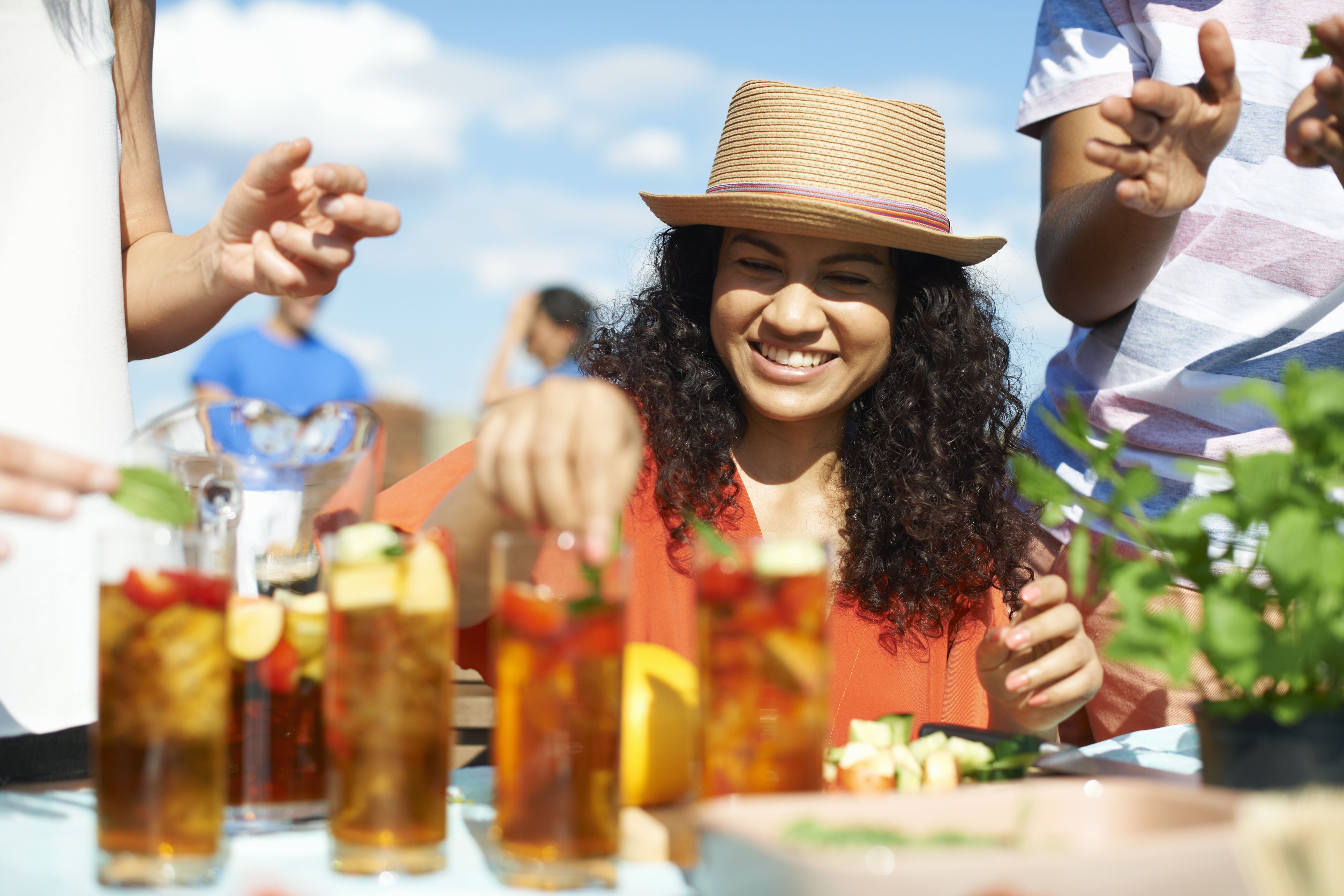 Woman in straw hat smiling at outdoor table with drinks and friends.