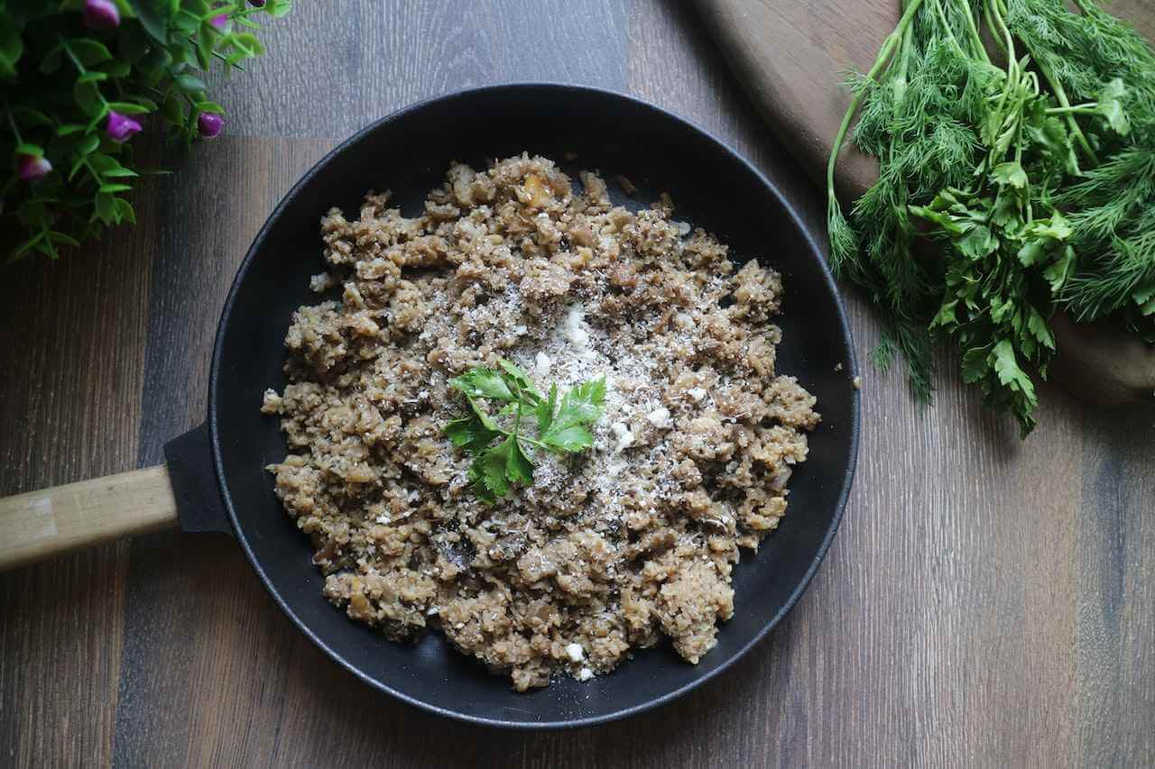 Cooked ground meat in a black skillet with fresh herbs and seasoning