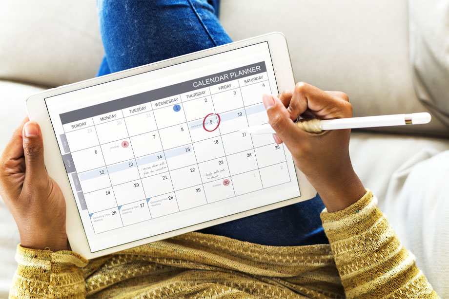 Person holding digital tablet displaying calendar planner with stylus pen marking dates