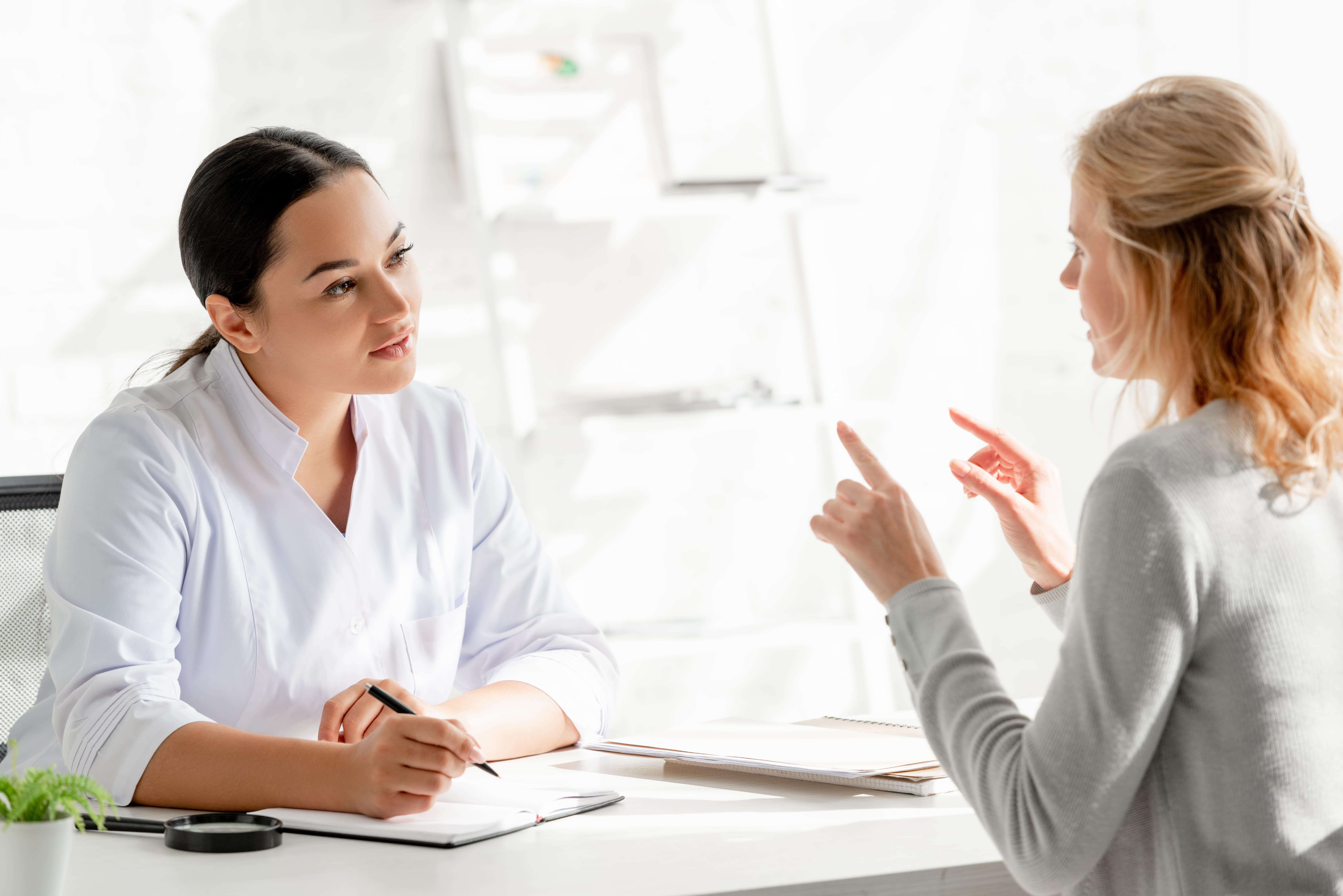 Two women having a professional conversation at a desk in a bright office.