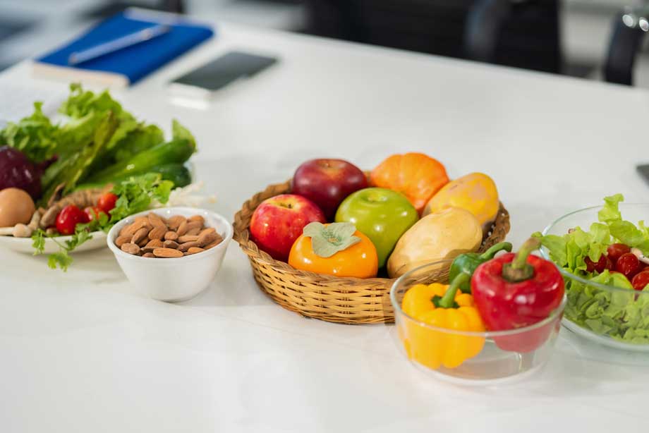 Fresh vegetables and fruits arranged on white table including apples, peppers, lettuce, and almonds