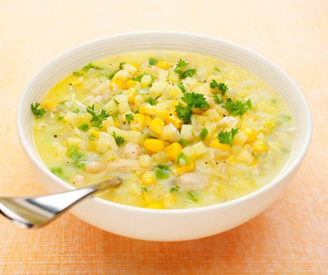 Creamy potato and corn chowder soup with green herbs in white bowl