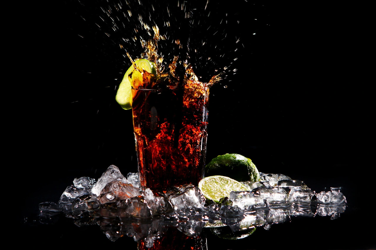 Glass of red drink splashing with ice, lime slices on black background