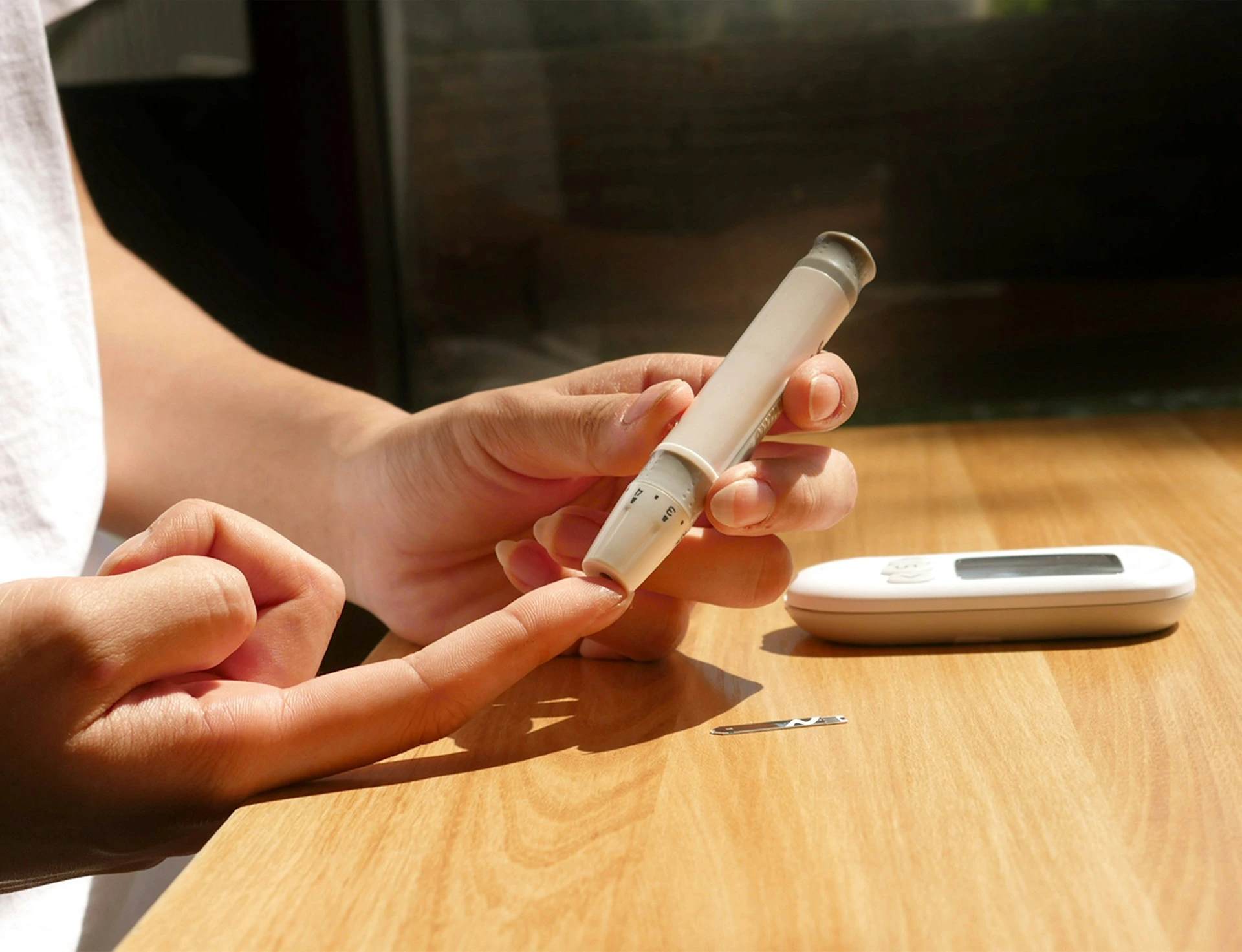 Person holding blood glucose meter and lancing device for diabetes testing on wooden table.