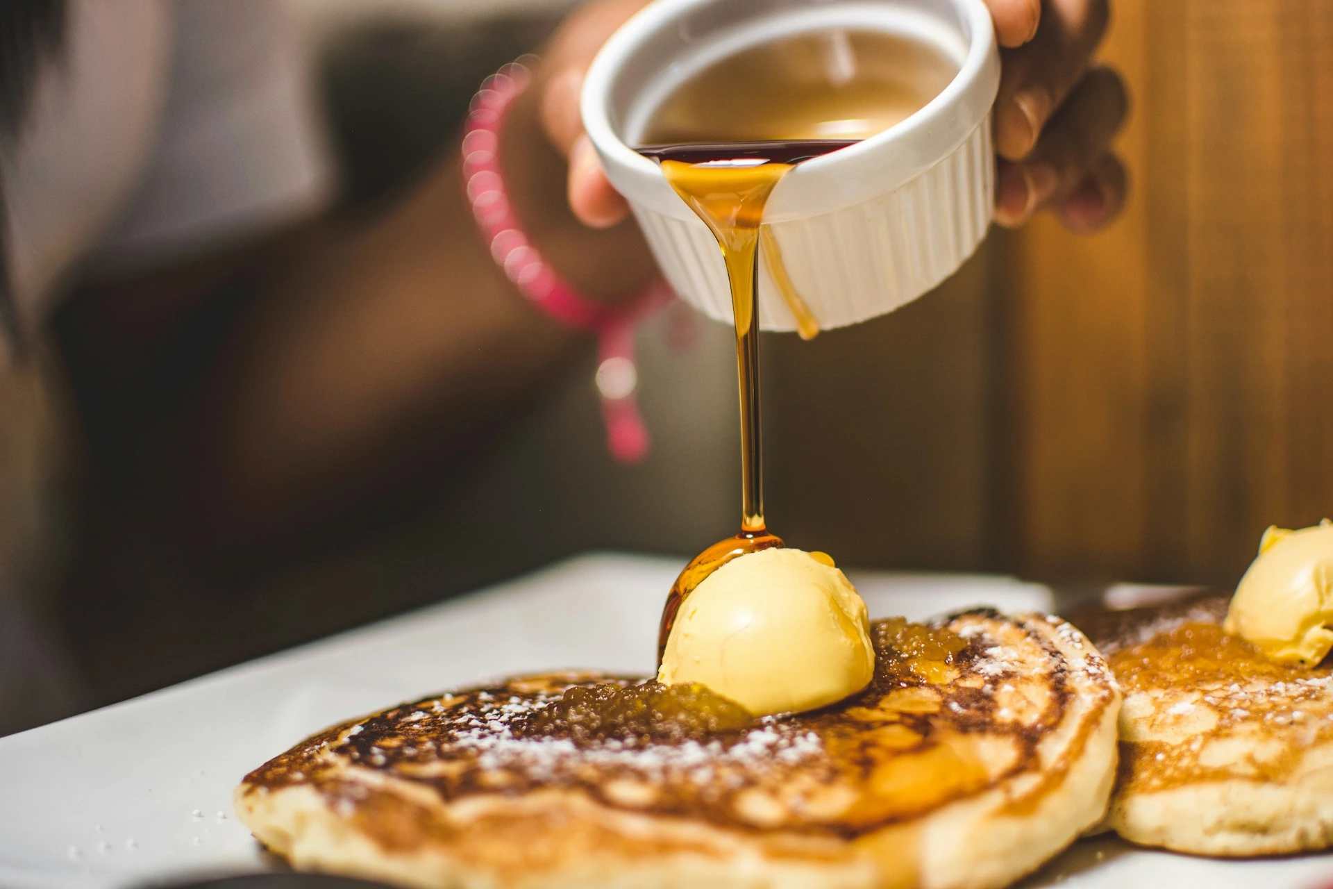 Golden honey drizzling onto warm pancakes with butter on white plate