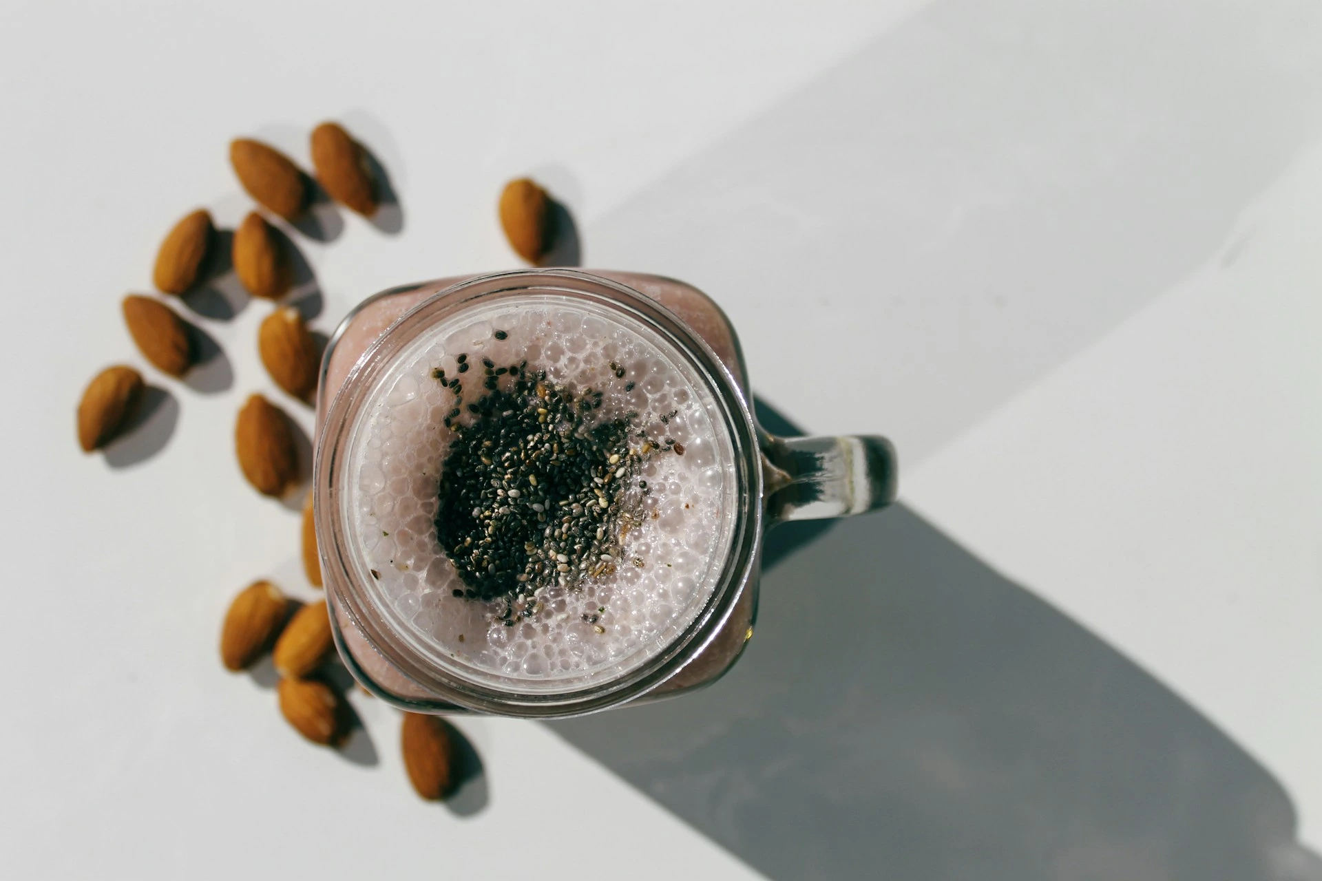 Almond milk smoothie with chia seeds in glass jar with almonds beside
