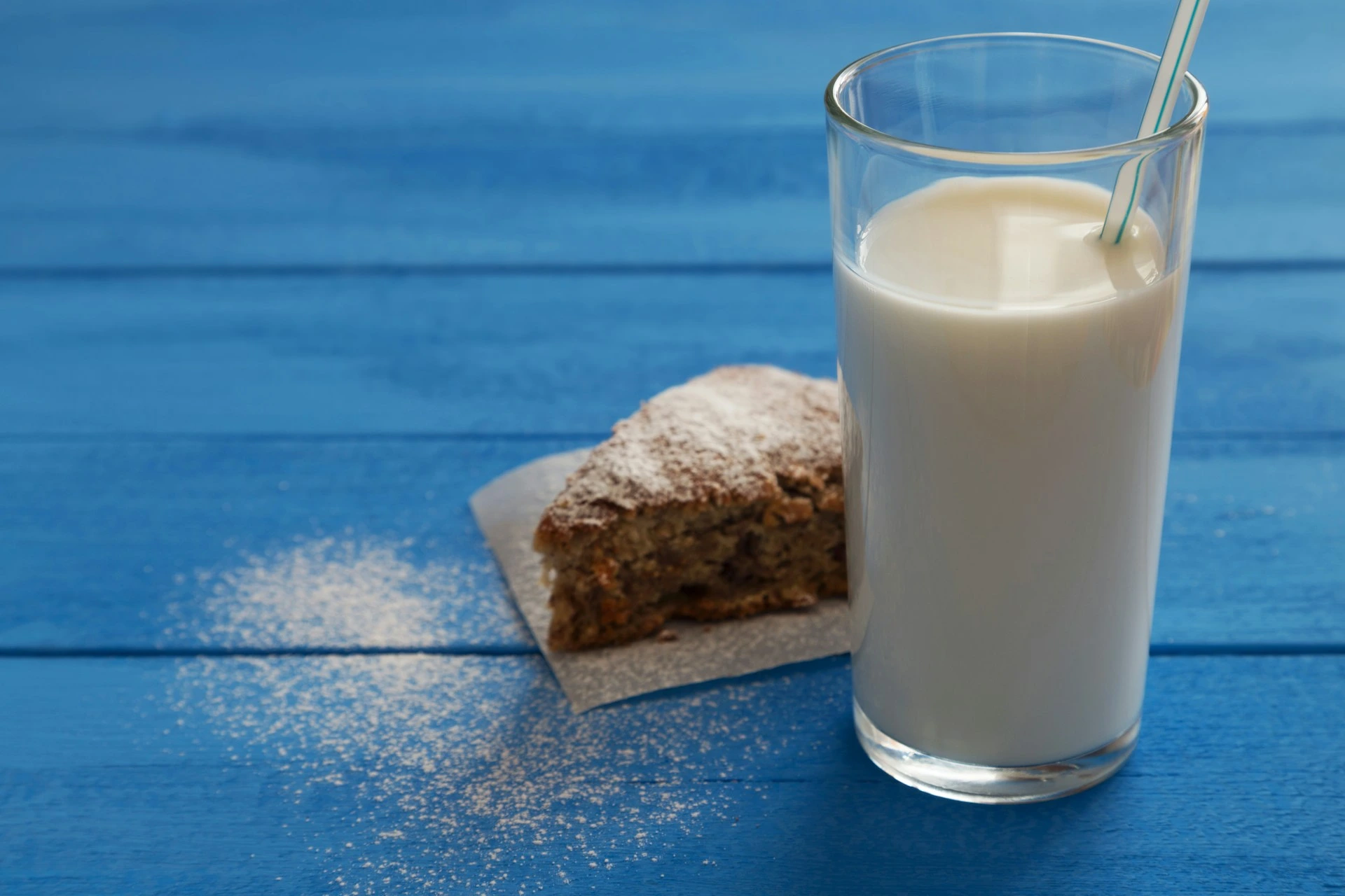 Glass of milk with slice of cake on blue wooden background