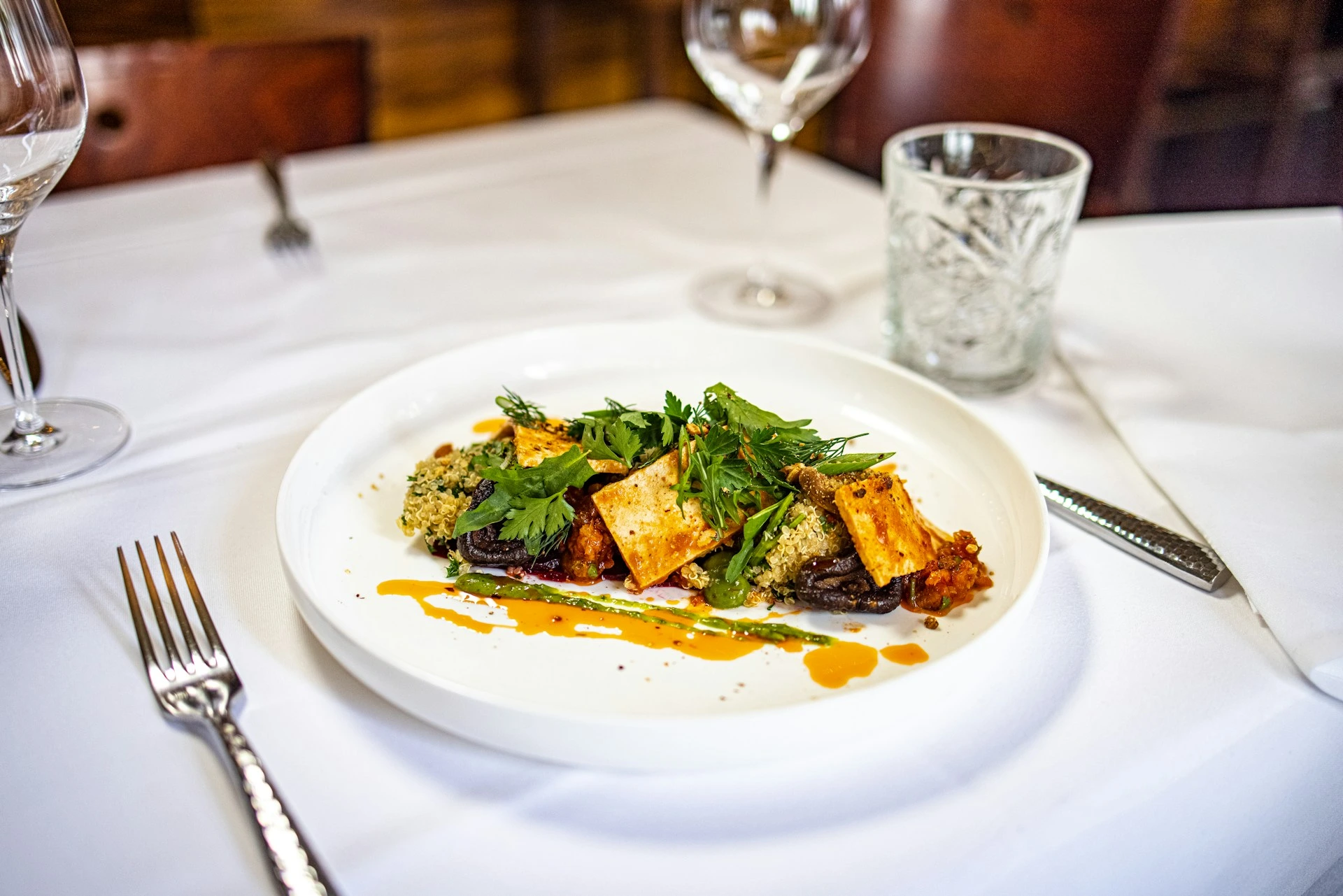 Gourmet plated dish with tofu, greens, and orange sauce on white plate