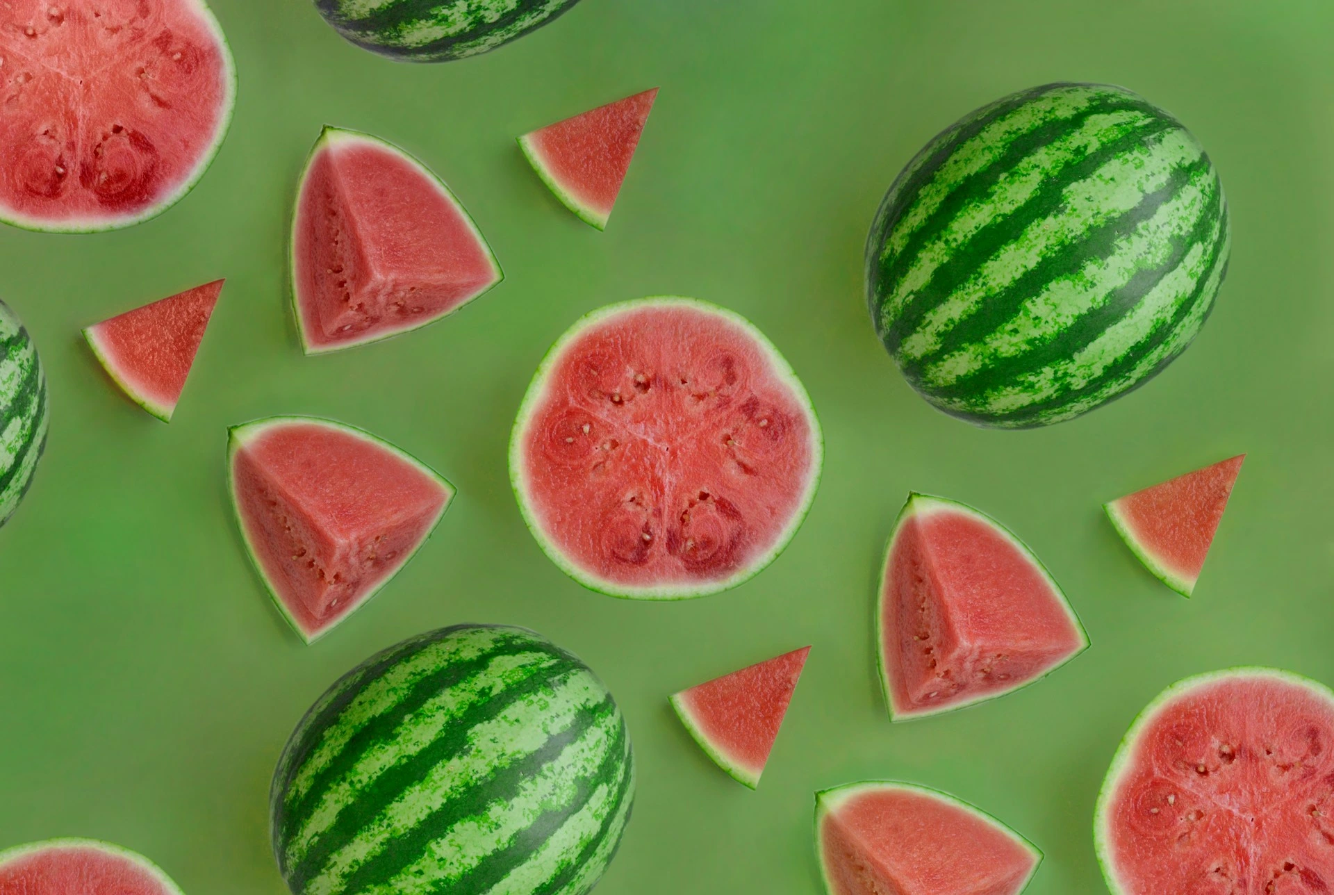 Whole and sliced red watermelons arranged on green background with whole green striped watermelons