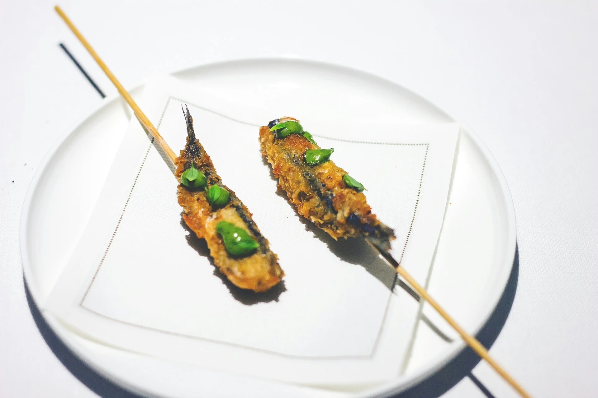 Two grilled seafood skewers with green onion garnish on white plate with chopsticks.