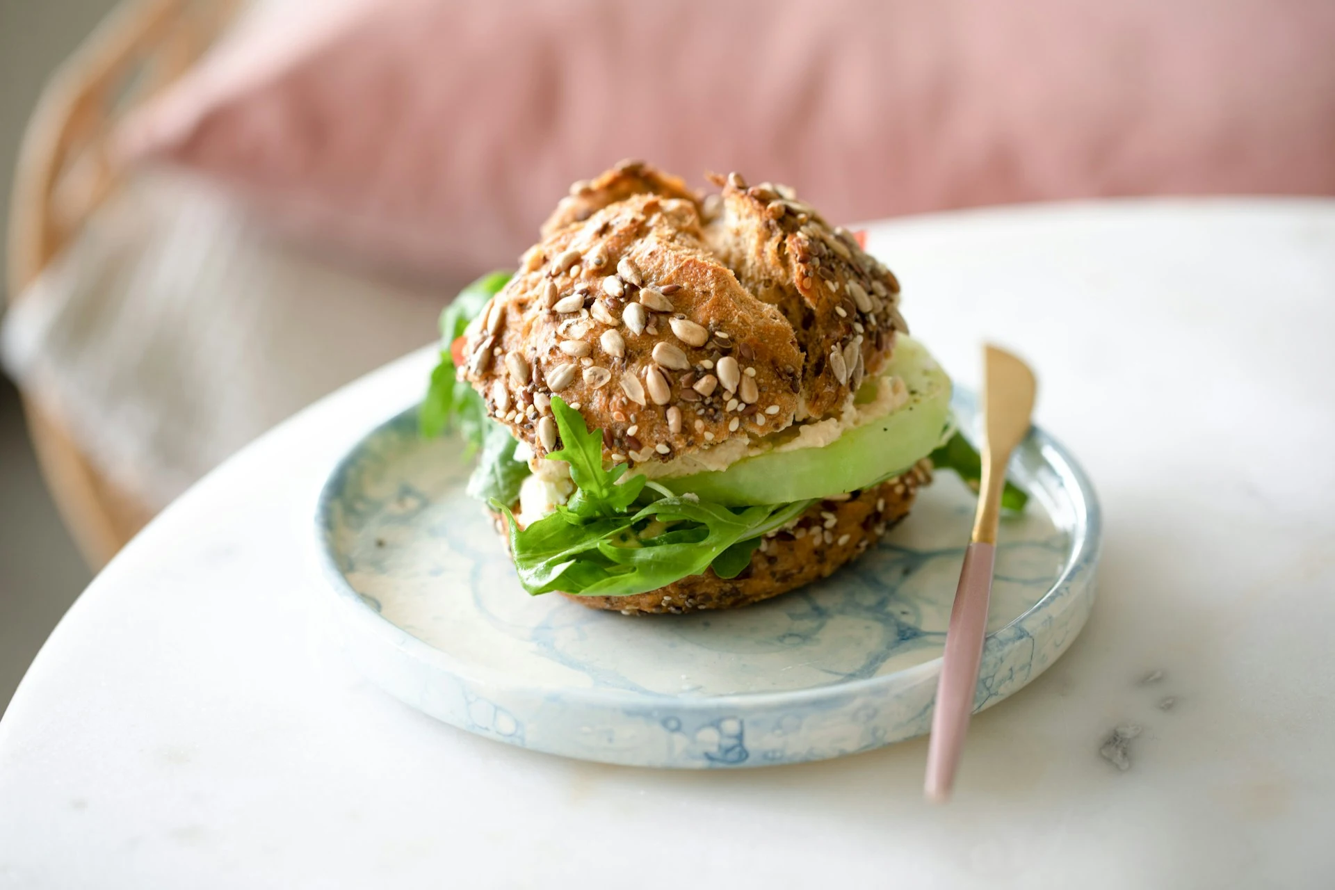 Seeded whole grain bagel with avocado and fresh greens on decorative plate