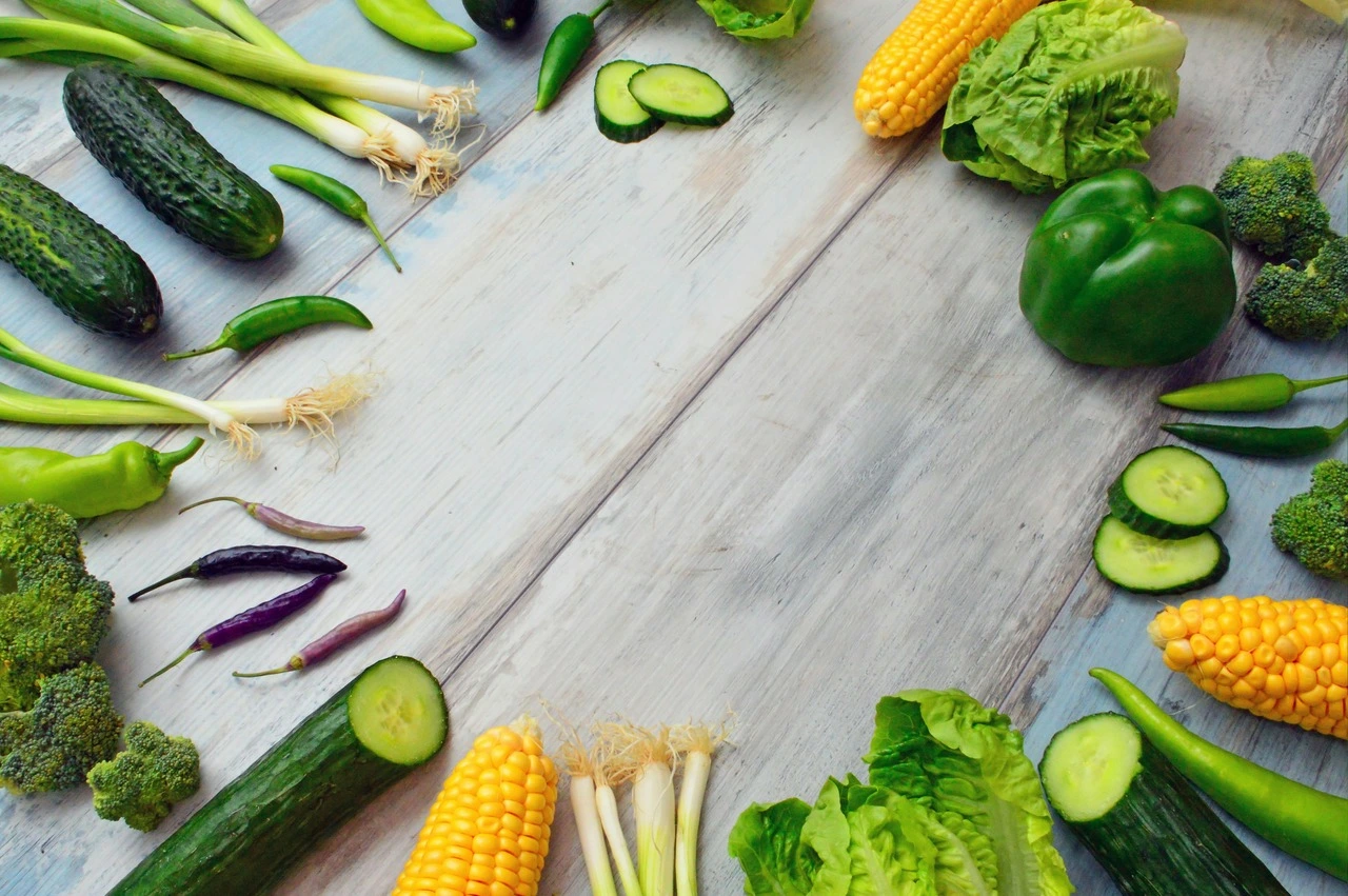 Fresh vegetables including cucumbers, corn, lettuce, peppers, and green onions on wooden surface.