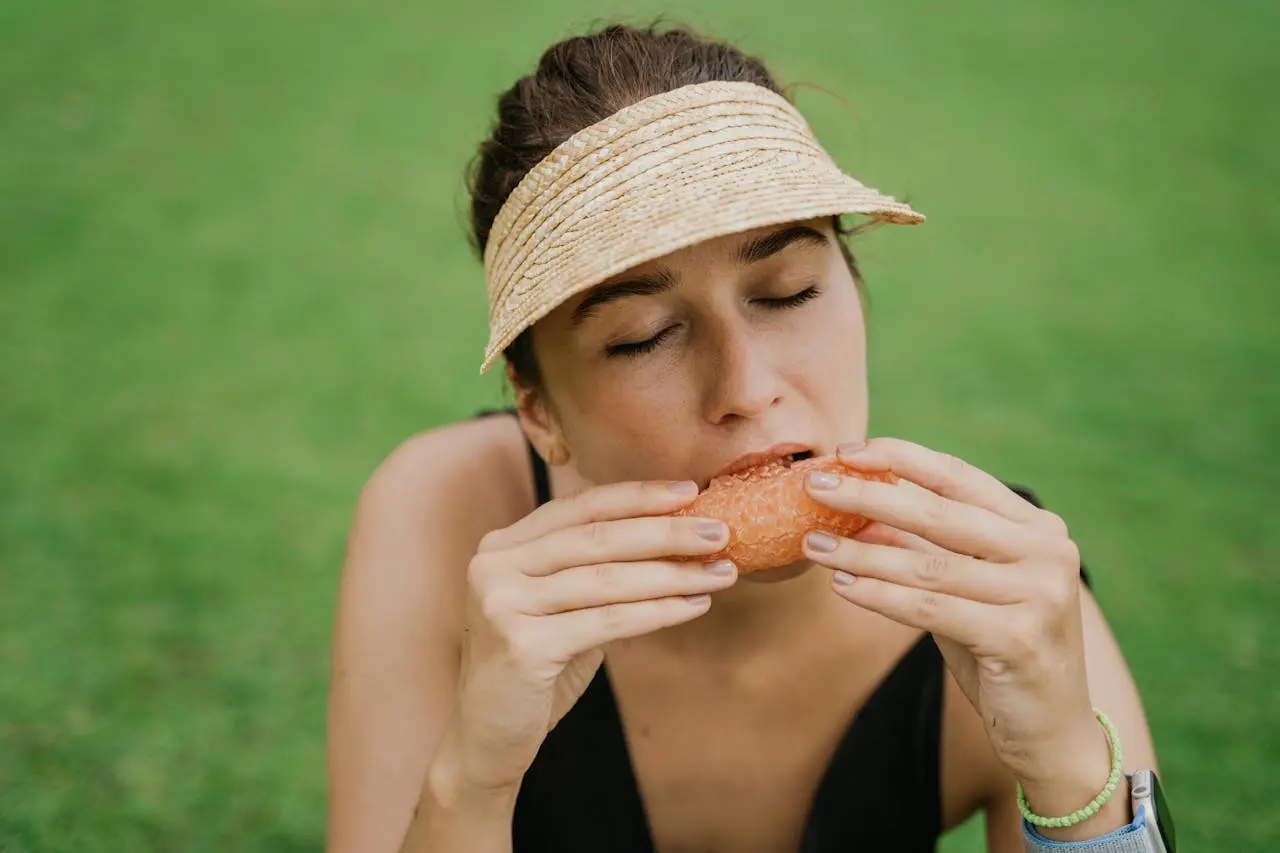 Person in straw visor eating juicy grapefruit with eyes closed outdoors