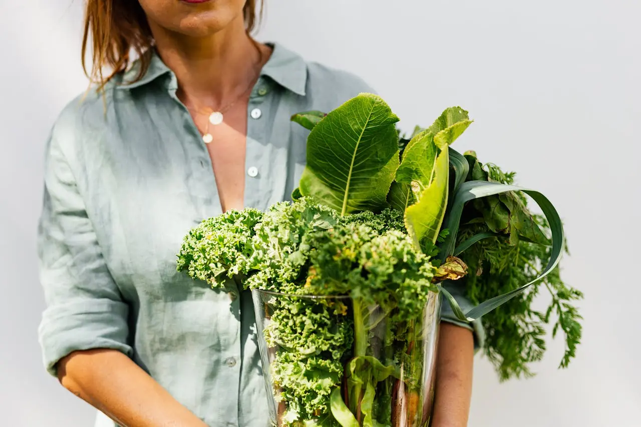 Person holding glass vase with fresh green leafy vegetables and herbs