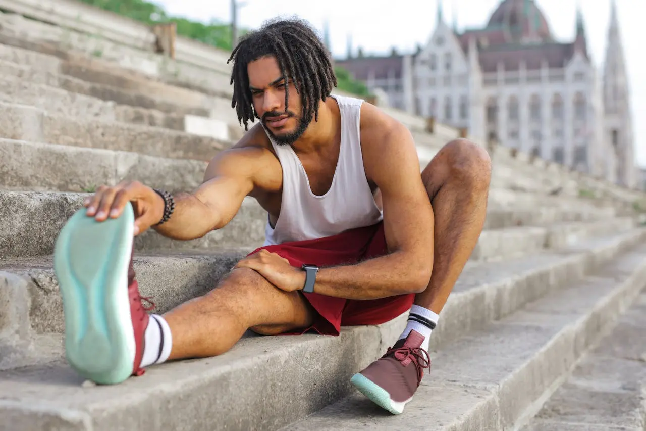 Athlete with dreadlocks stretching on stone steps before urban workout