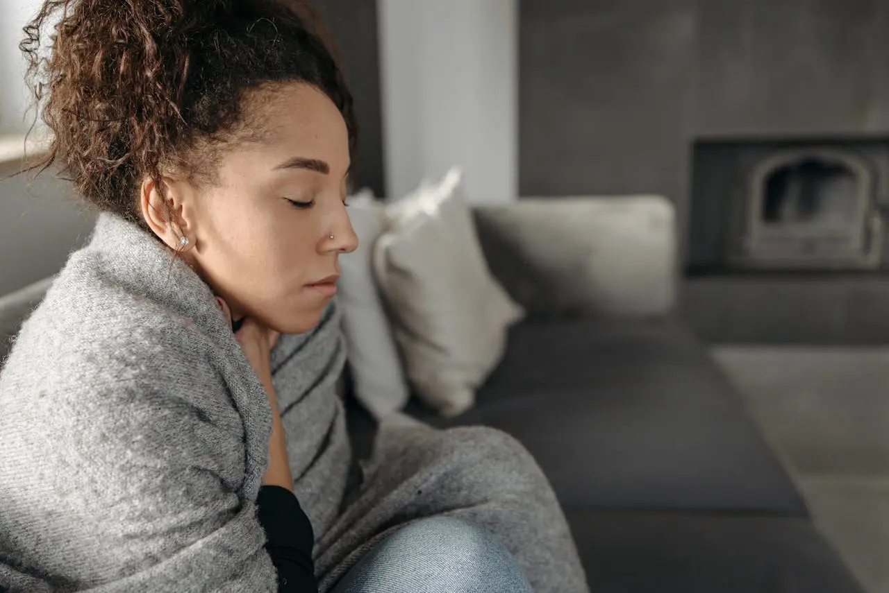 Woman with curly hair sitting on couch looking down pensively indoors
