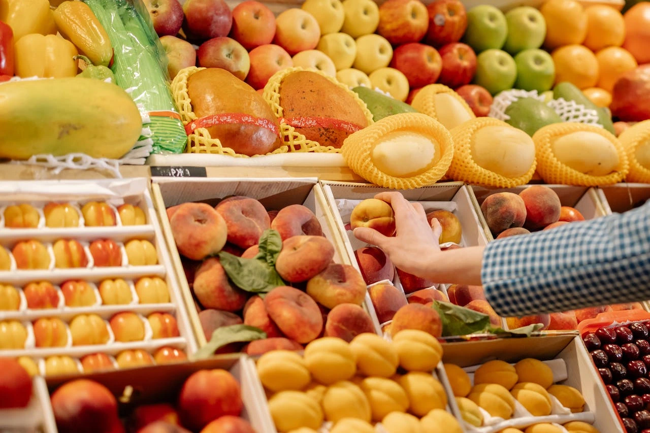 Customer selecting fresh fruit at farmers market with colorful displays of apples, pears, and citrus